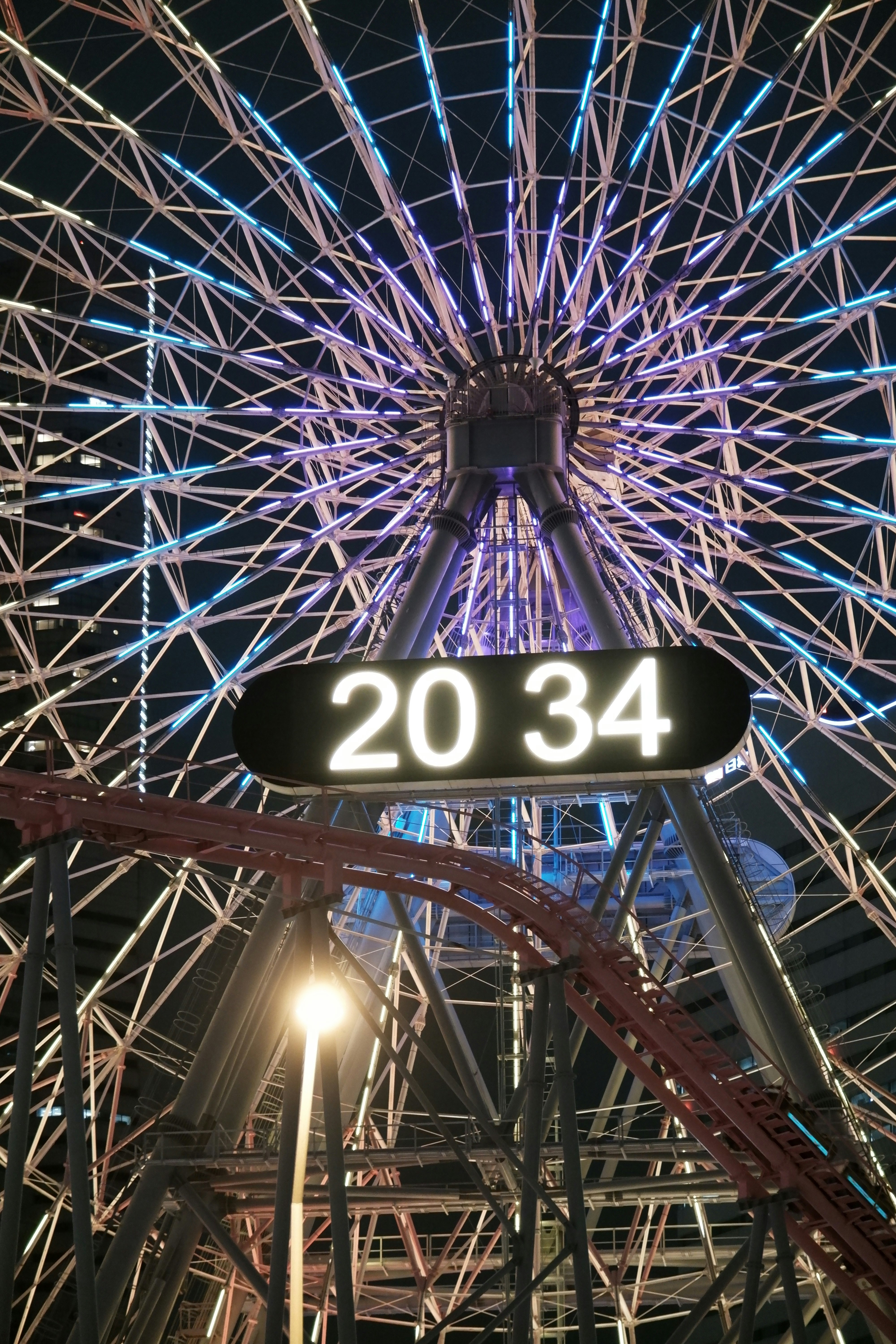 巨大な放射状の構造と「20 34」の表示がある夜の遊園地の観覧施設