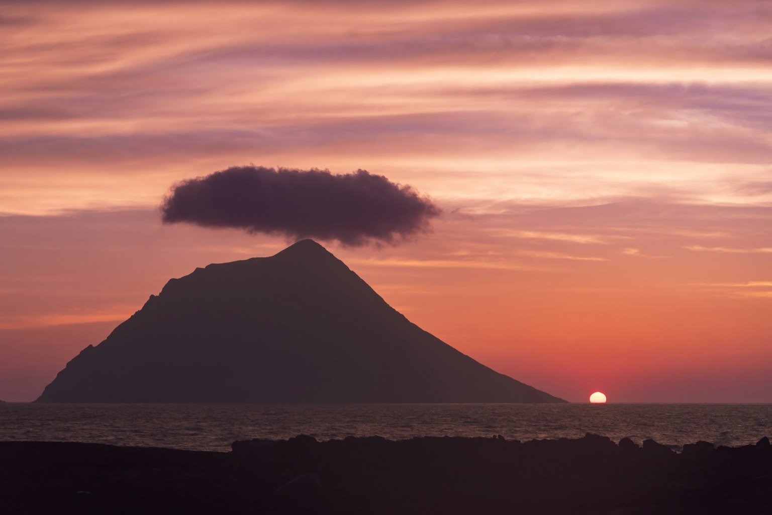 Silhouette of a mountain with a cloud at sunset