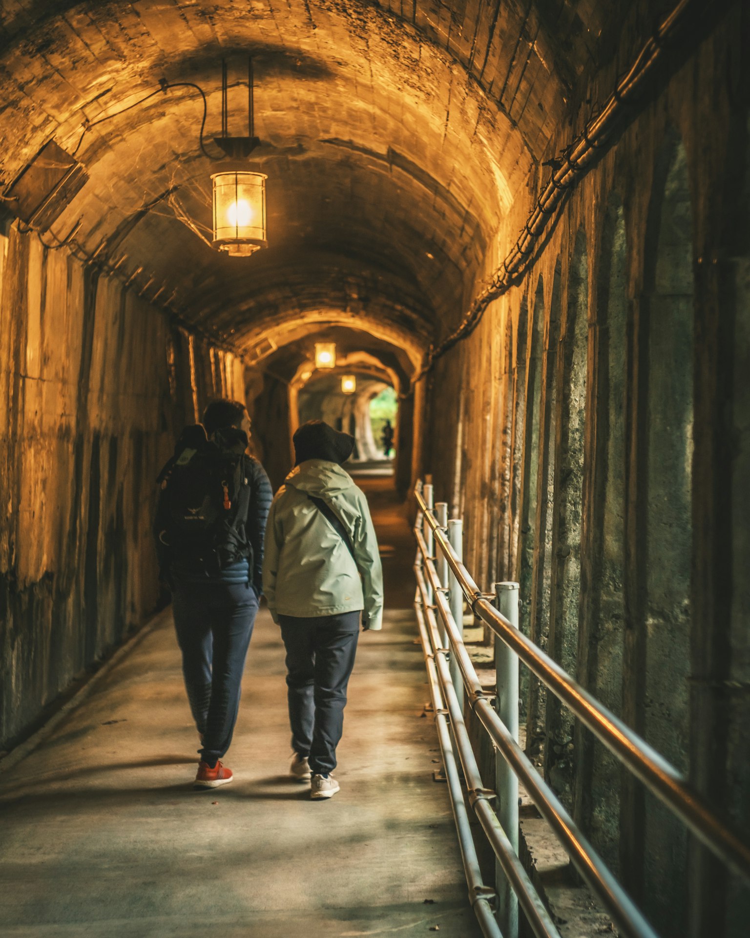 Two people walking in a dimly lit tunnel Warm light fixtures create a unique atmosphere