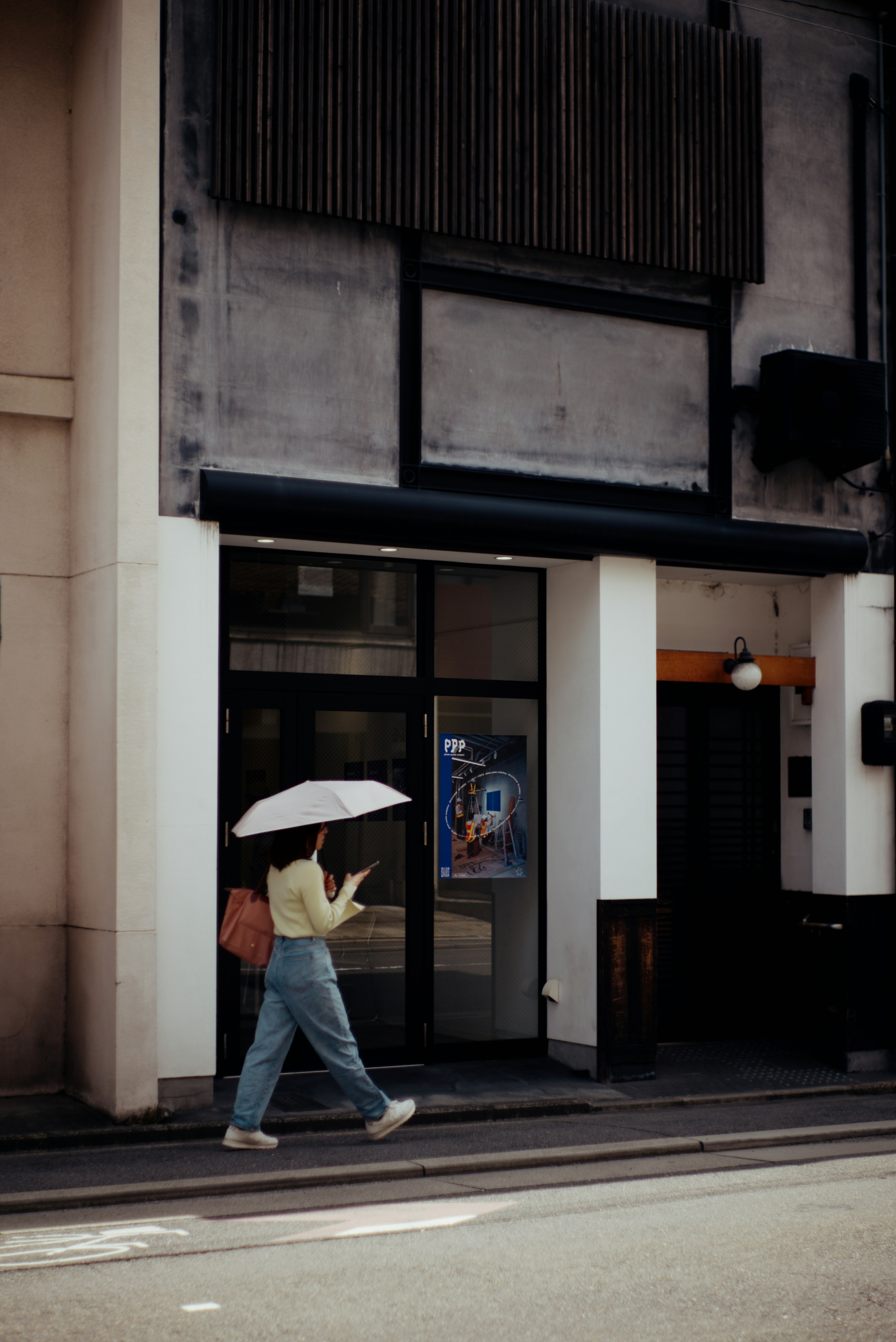 Woman walking with an umbrella in front of a simple building