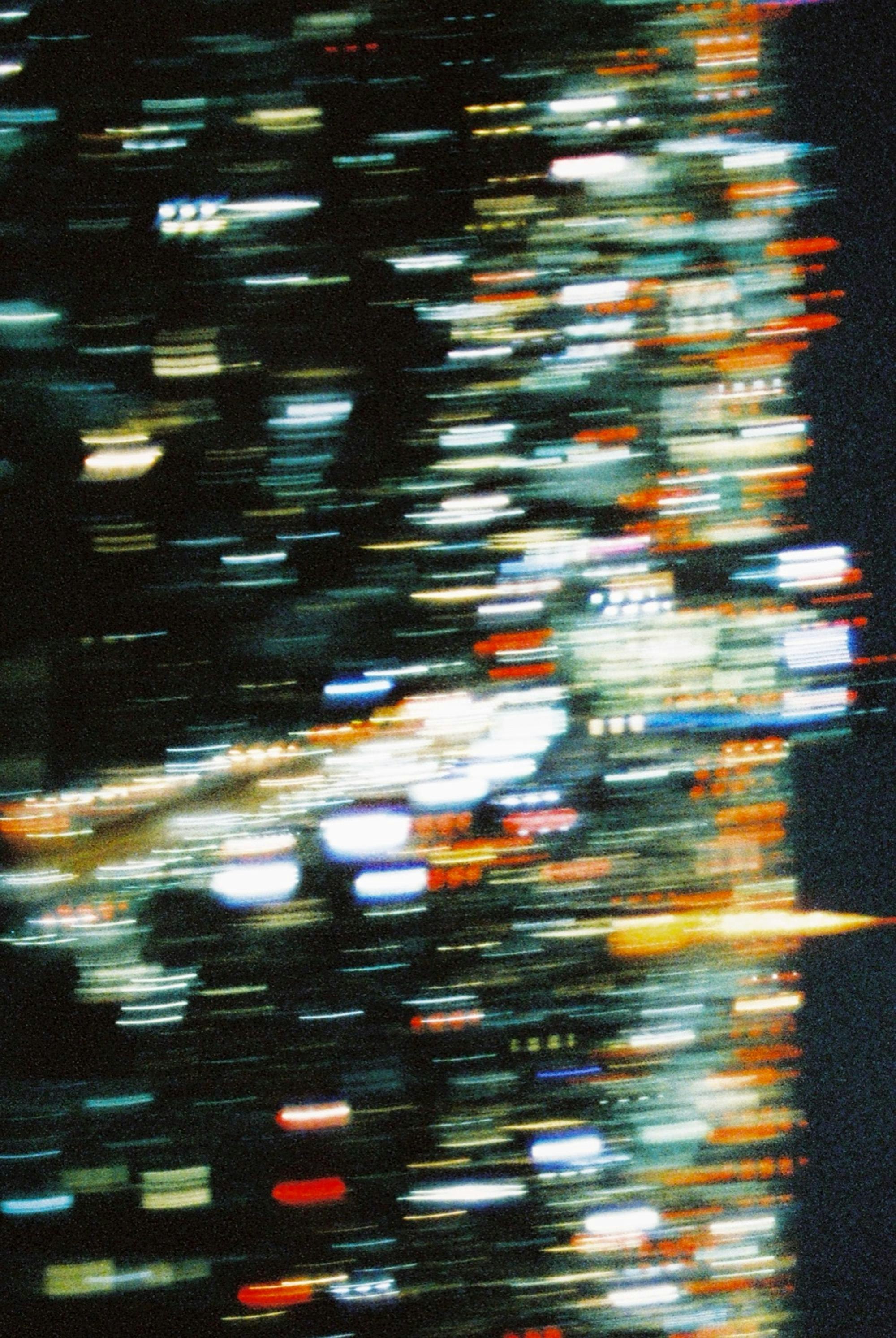 夜の高速道路のような光の流れがにじむ都市の風景