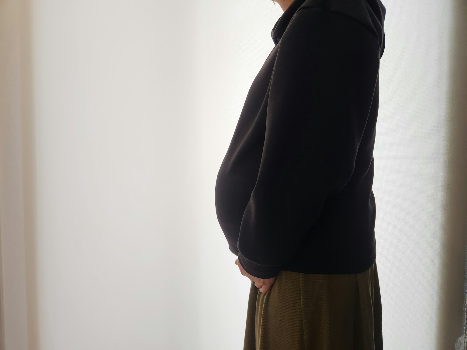 Silhouette of a pregnant woman in profile wearing a black hooded jacket and green skirt bright background