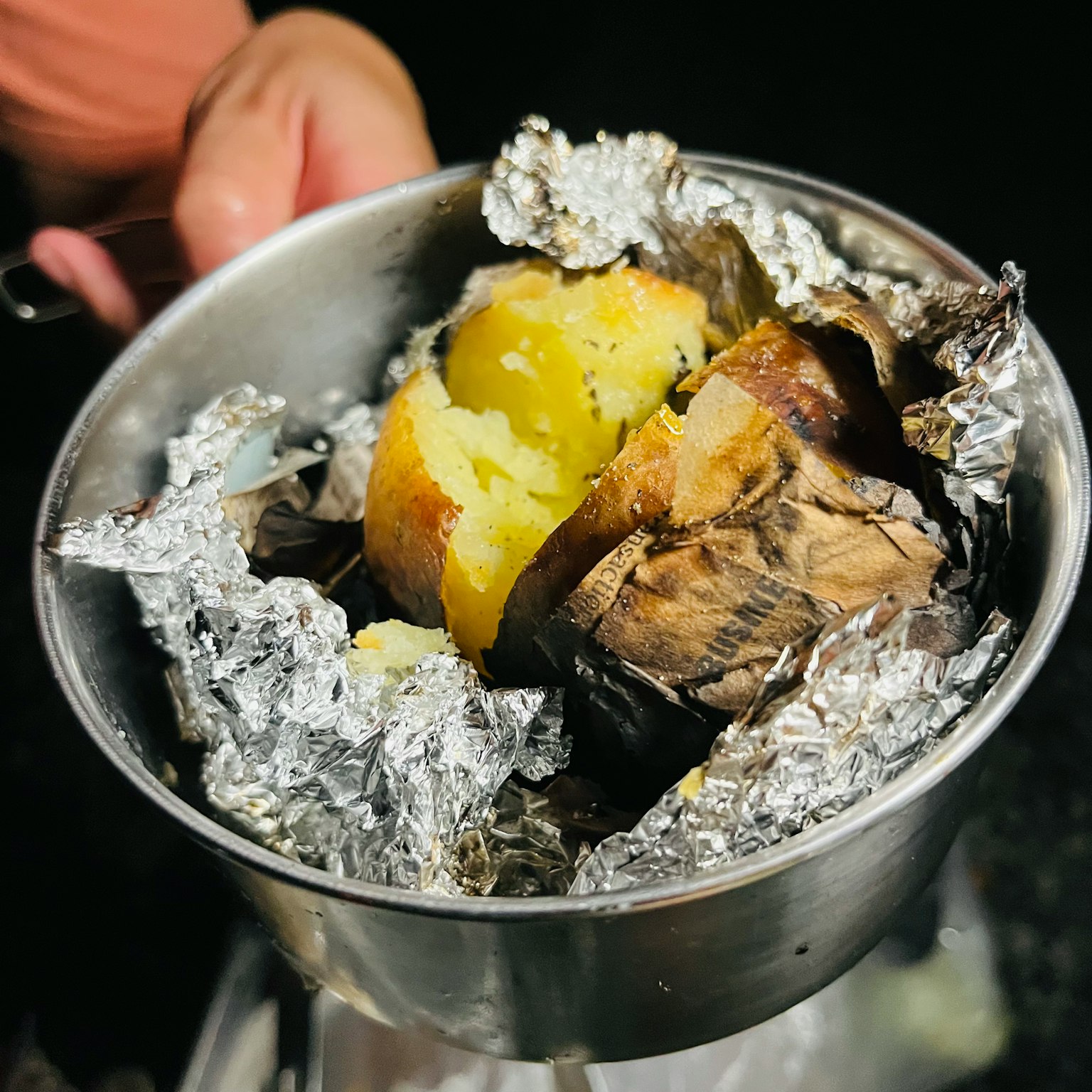 Una pentola tenuta in mano contenente patate dolci al forno avvolte in foglio di alluminio