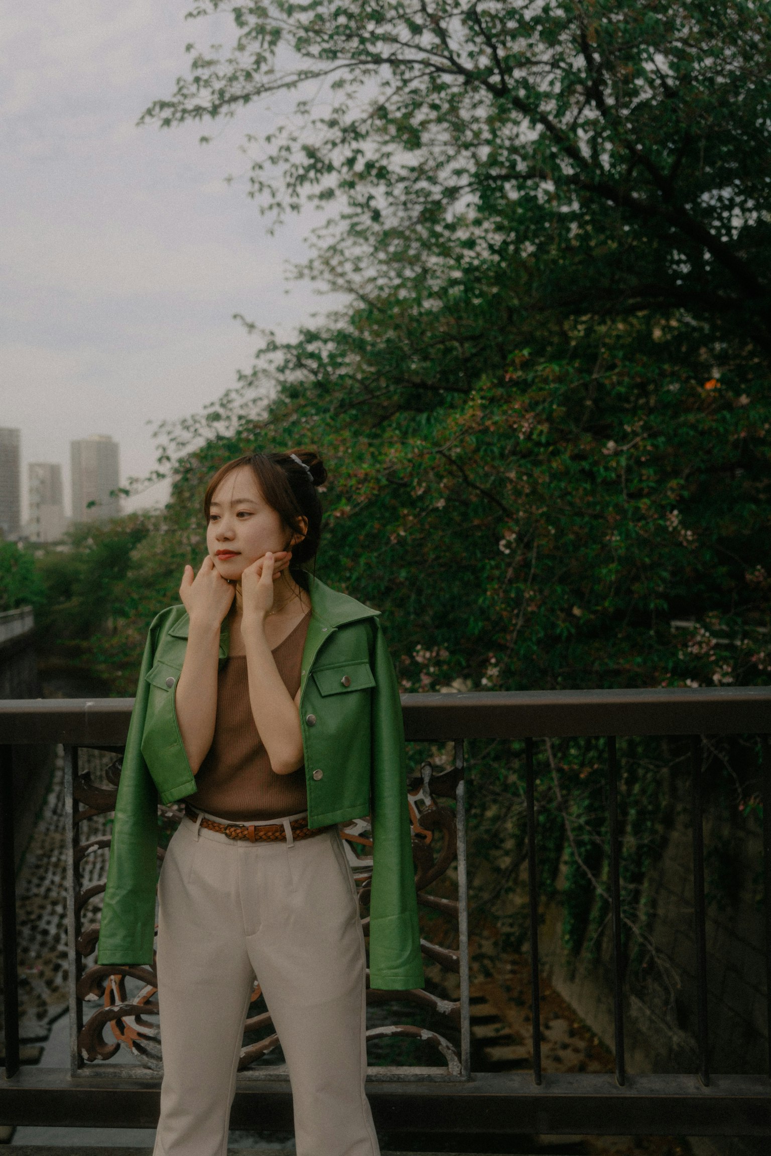 穿着绿色夹克的女性站在桥上，背景是绿色植物