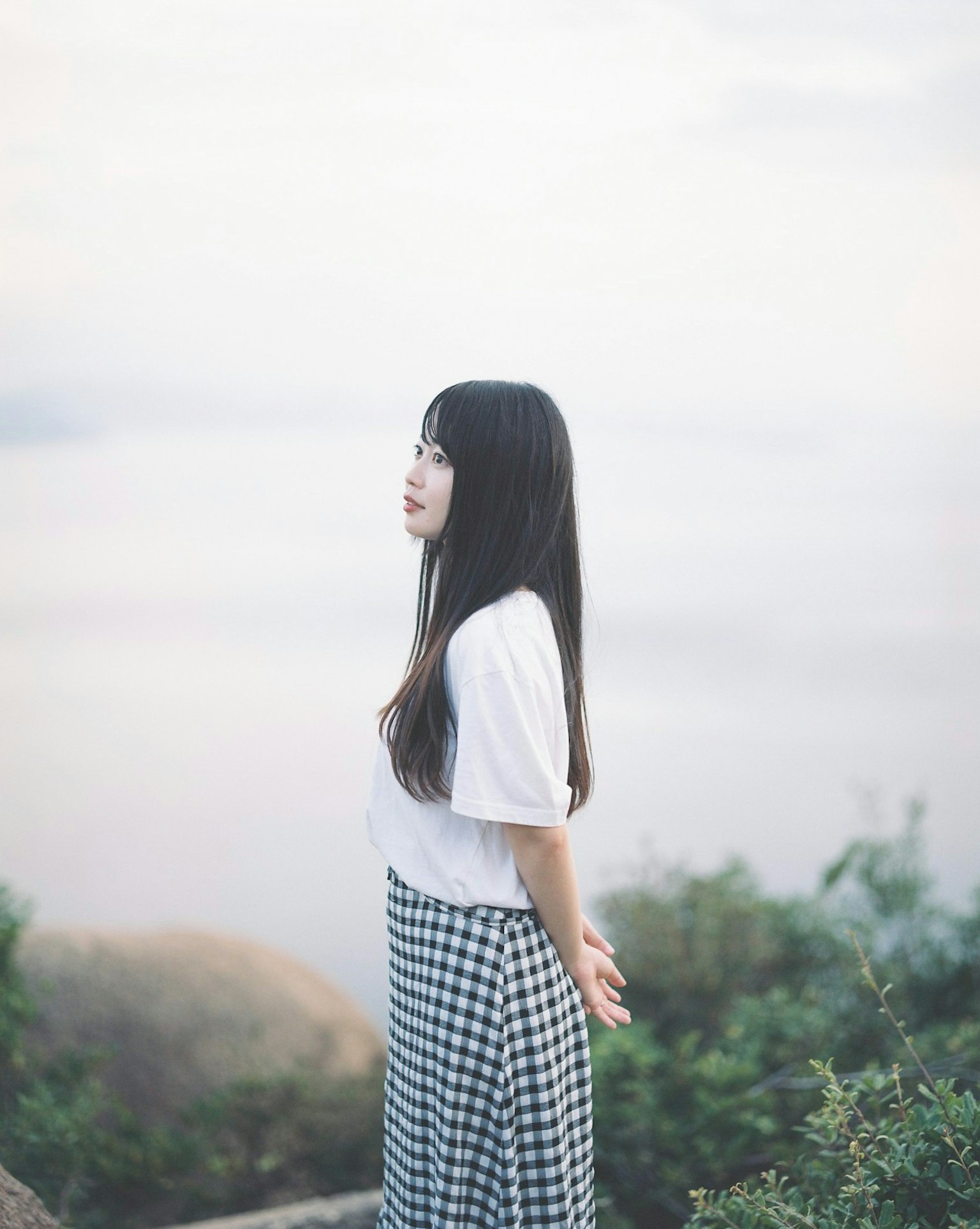 一位女性静静地站在湖边穿着白色T恤和格子裙