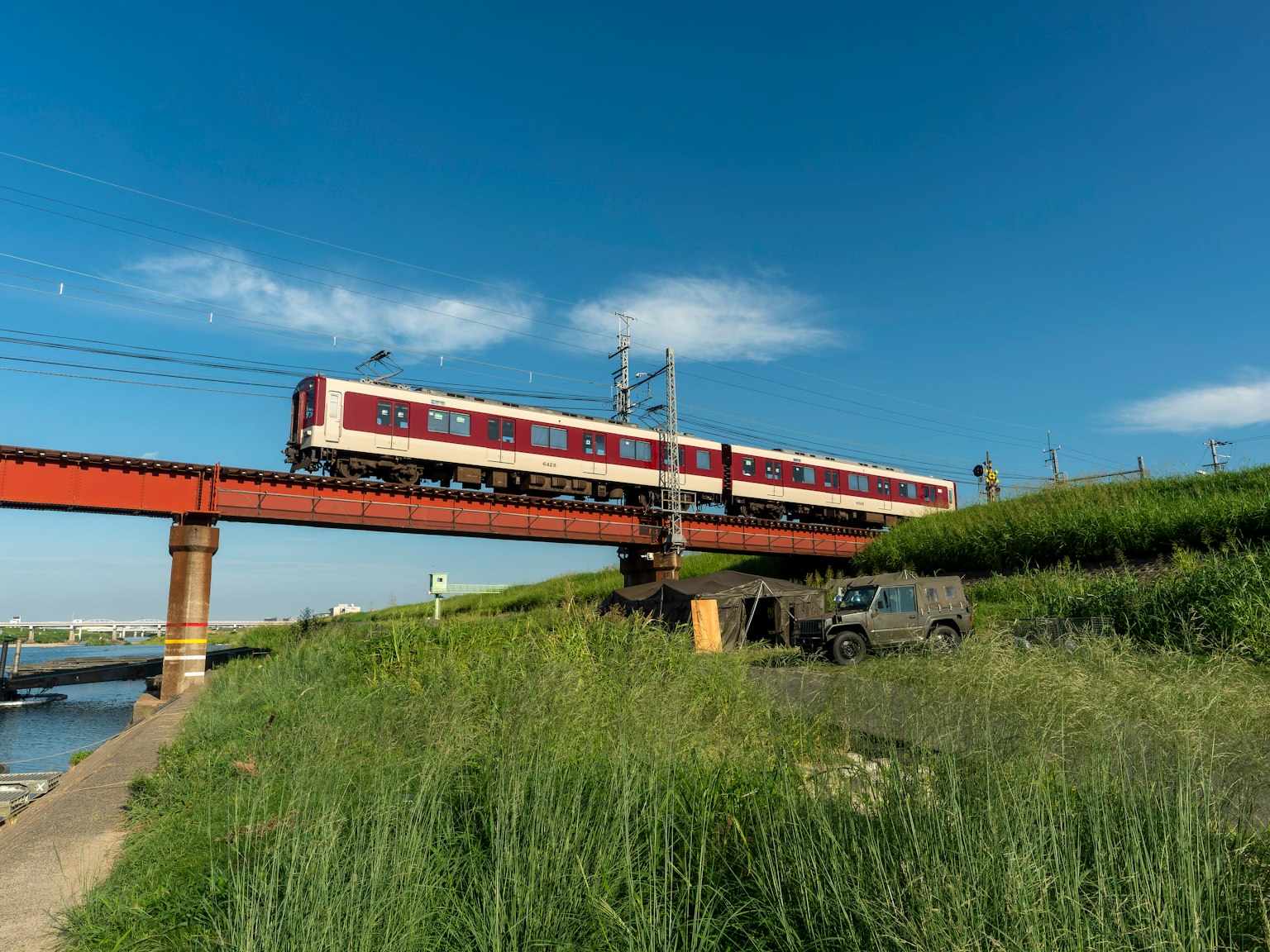 Train rouge traversant un pont au-dessus d'une rivière sous un ciel bleu