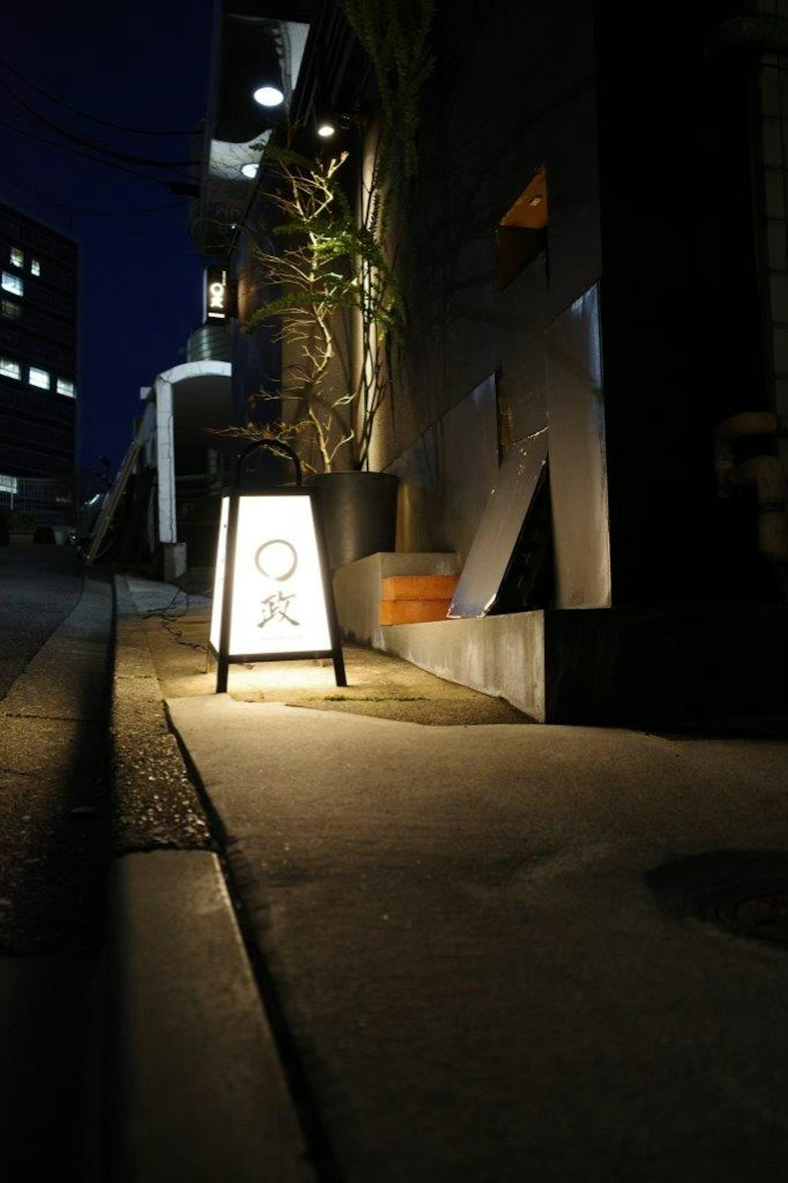 Papan yang diterangi di trotoar pada malam hari dengan latar belakang perkotaan