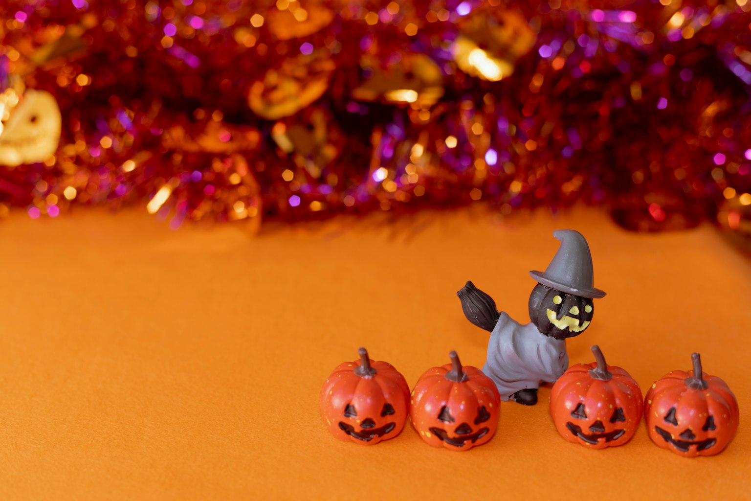 Une scène d'Halloween avec une figurine de sorcière et quatre citrouilles sculptées sur un fond orange