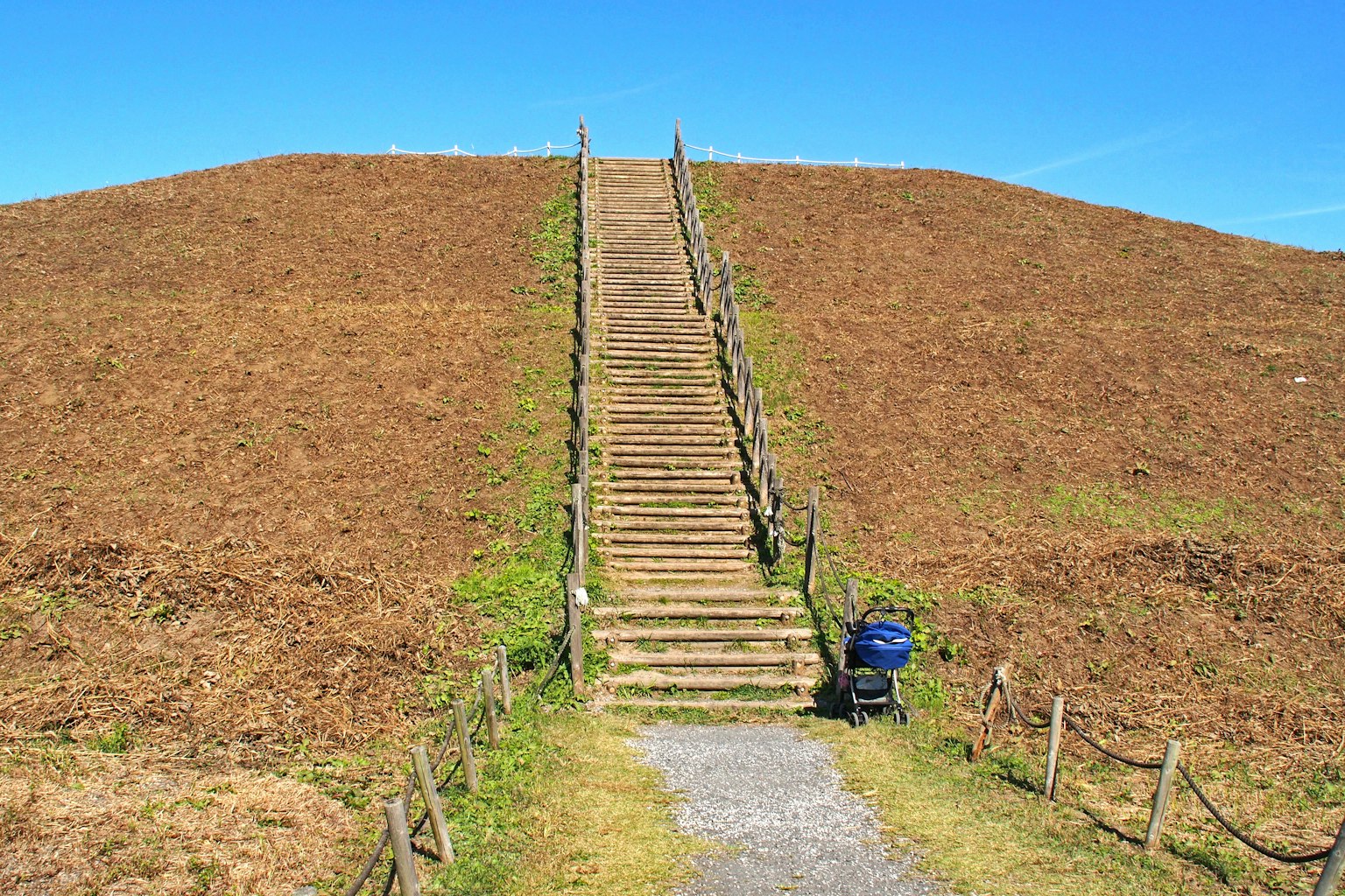 Vista de escaleras de madera que conducen a una colina marrón bajo un cielo azul claro