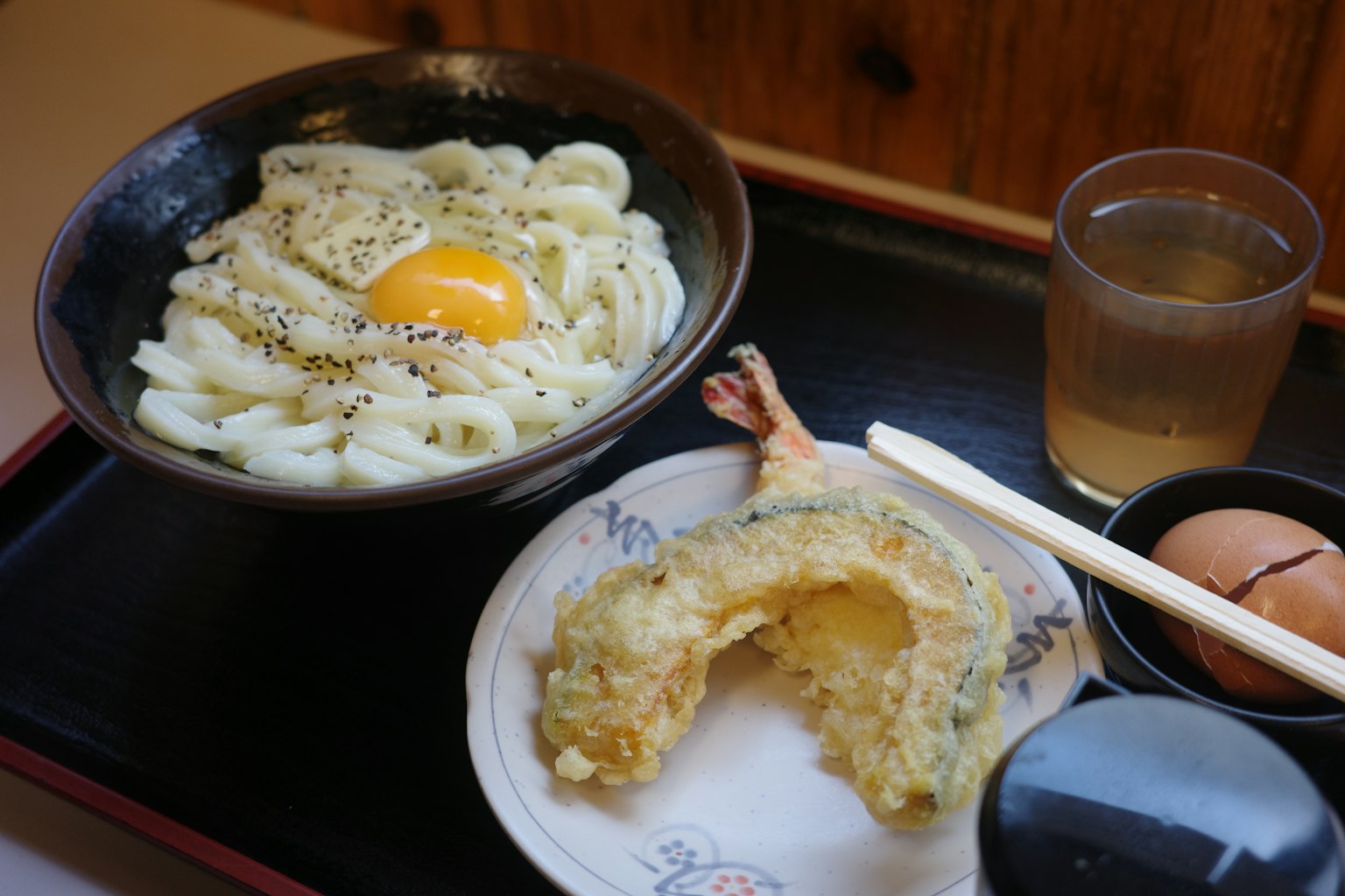 Un tazón de udon con huevo y tempura en un plato con una bebida