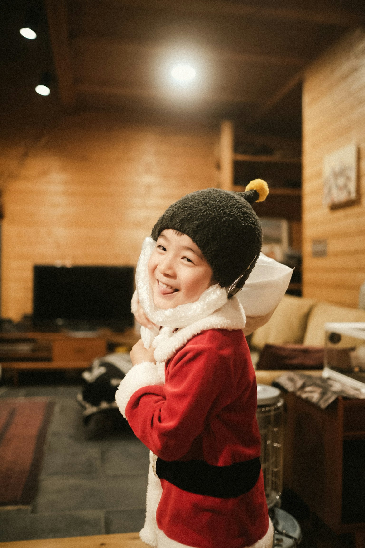 Enfant en costume de Père Noël rouge souriant et posant à l'intérieur