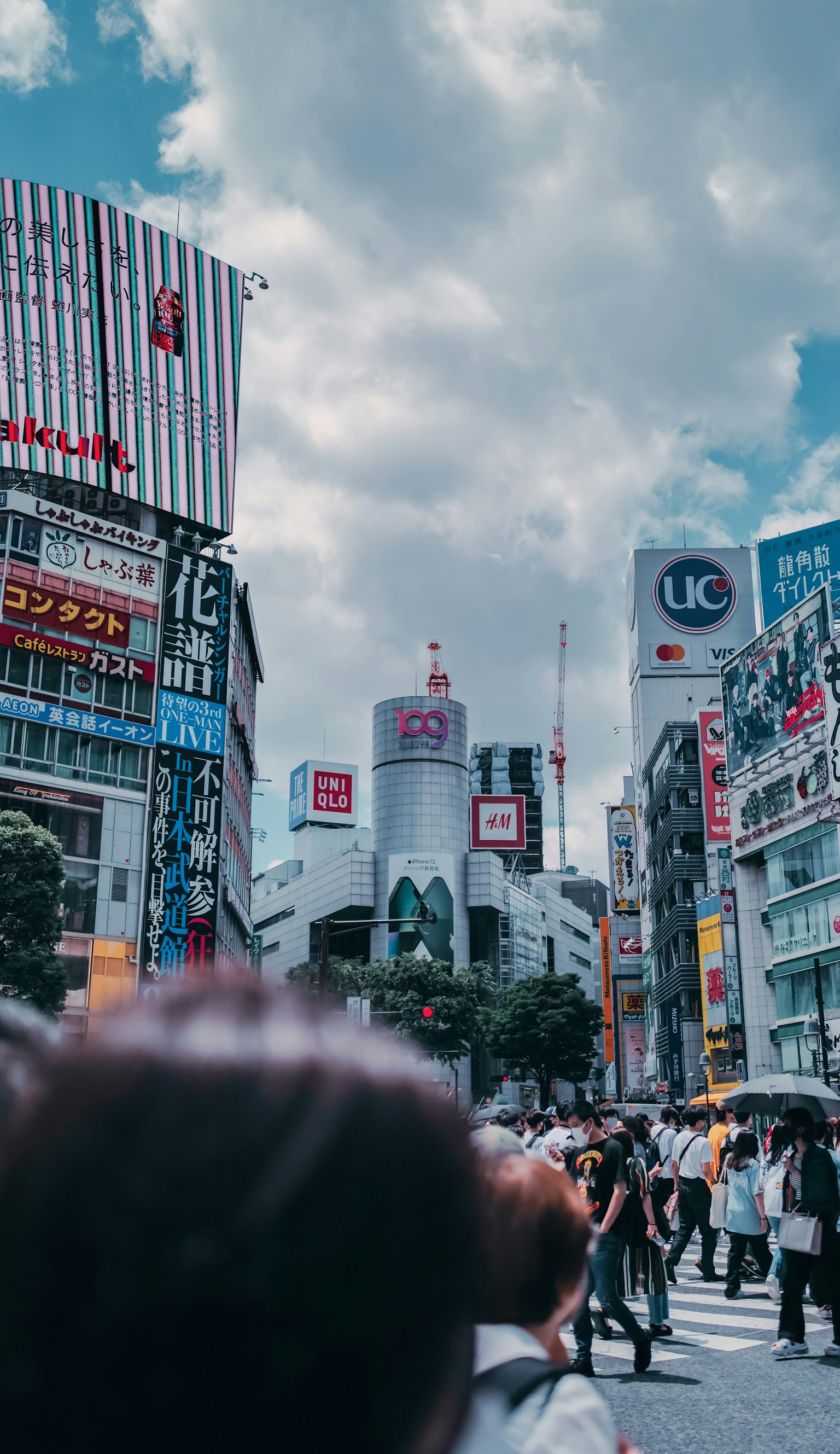 Kerumunan di persimpangan Shibuya dengan gedung tinggi di bawah langit biru