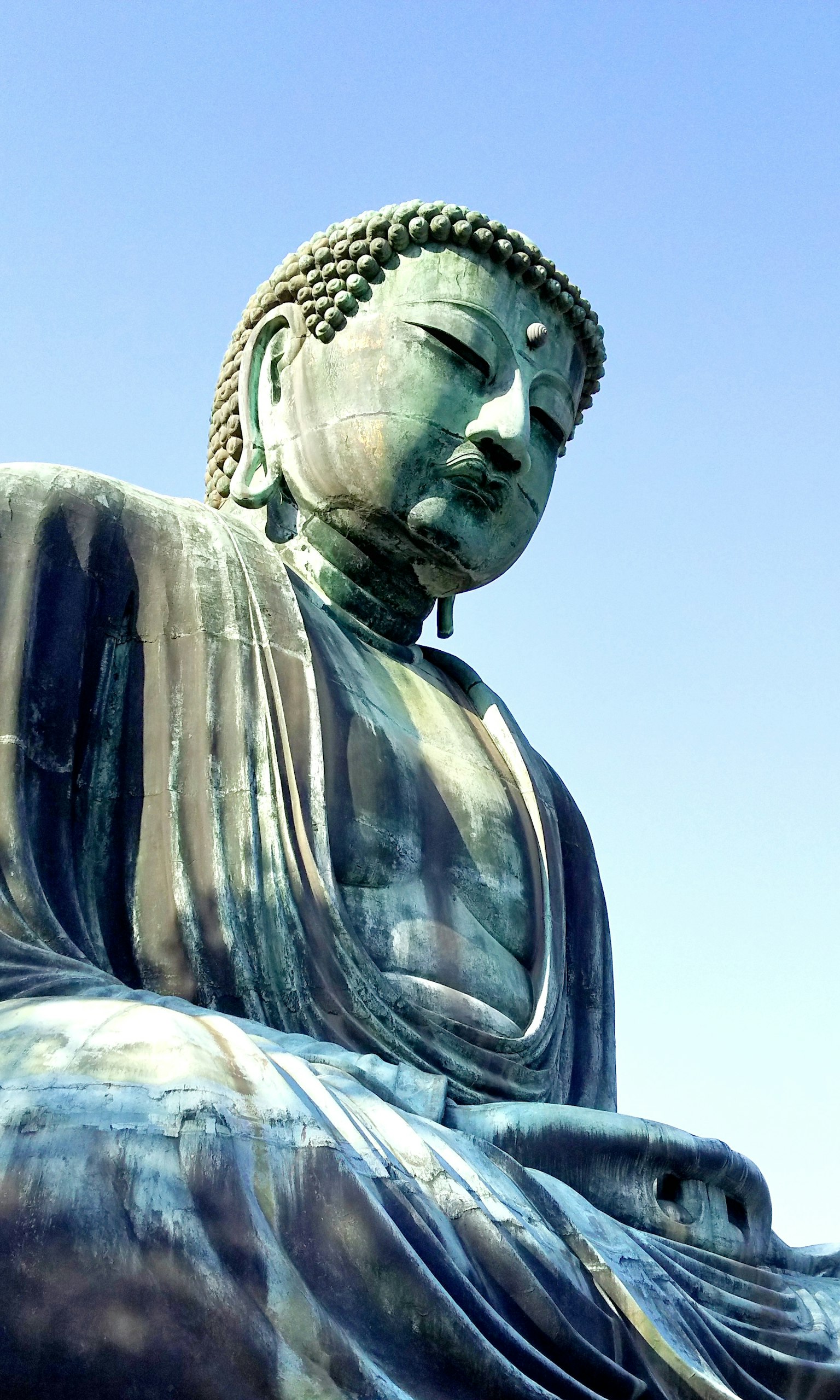 Tampak samping patung Buddha besar di bawah langit biru