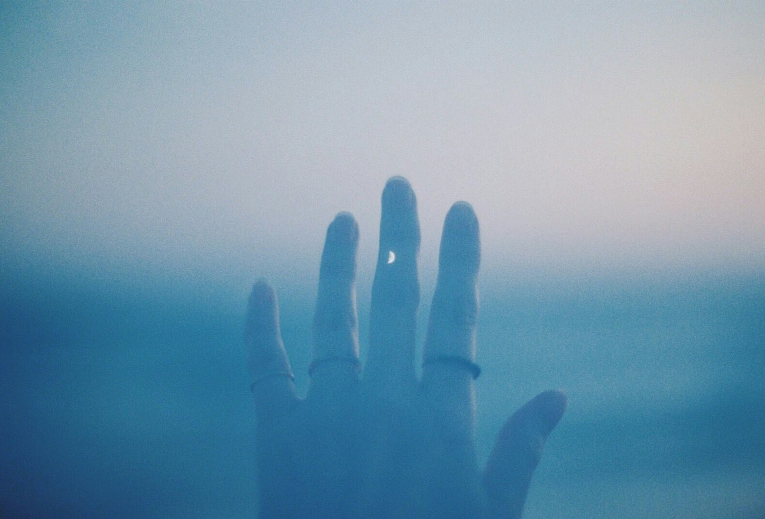 Silhouette einer Hand, die sich in Richtung eines blauen Ozeans mit Ringen an den Fingern ausstreckt