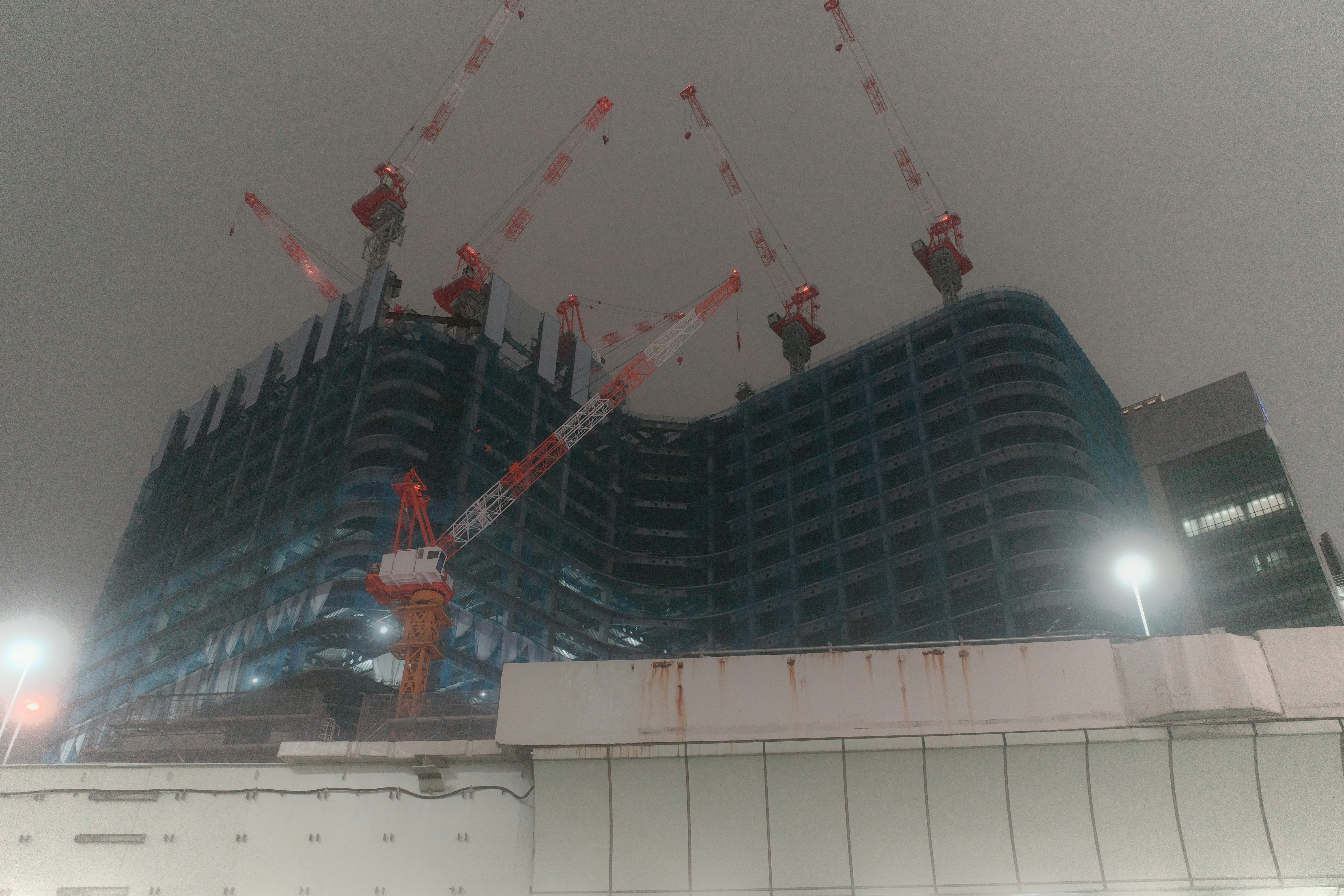 Night view of a construction site featuring cranes and blue tarps on a building