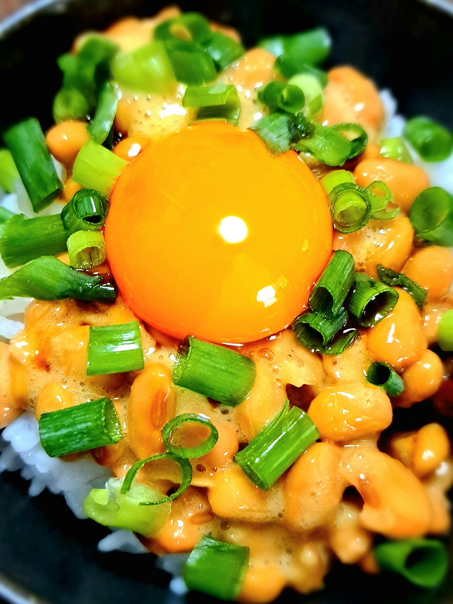 Un bol de riz surmonté d'un jaune d'œuf brillant et d'oignons verts hachés