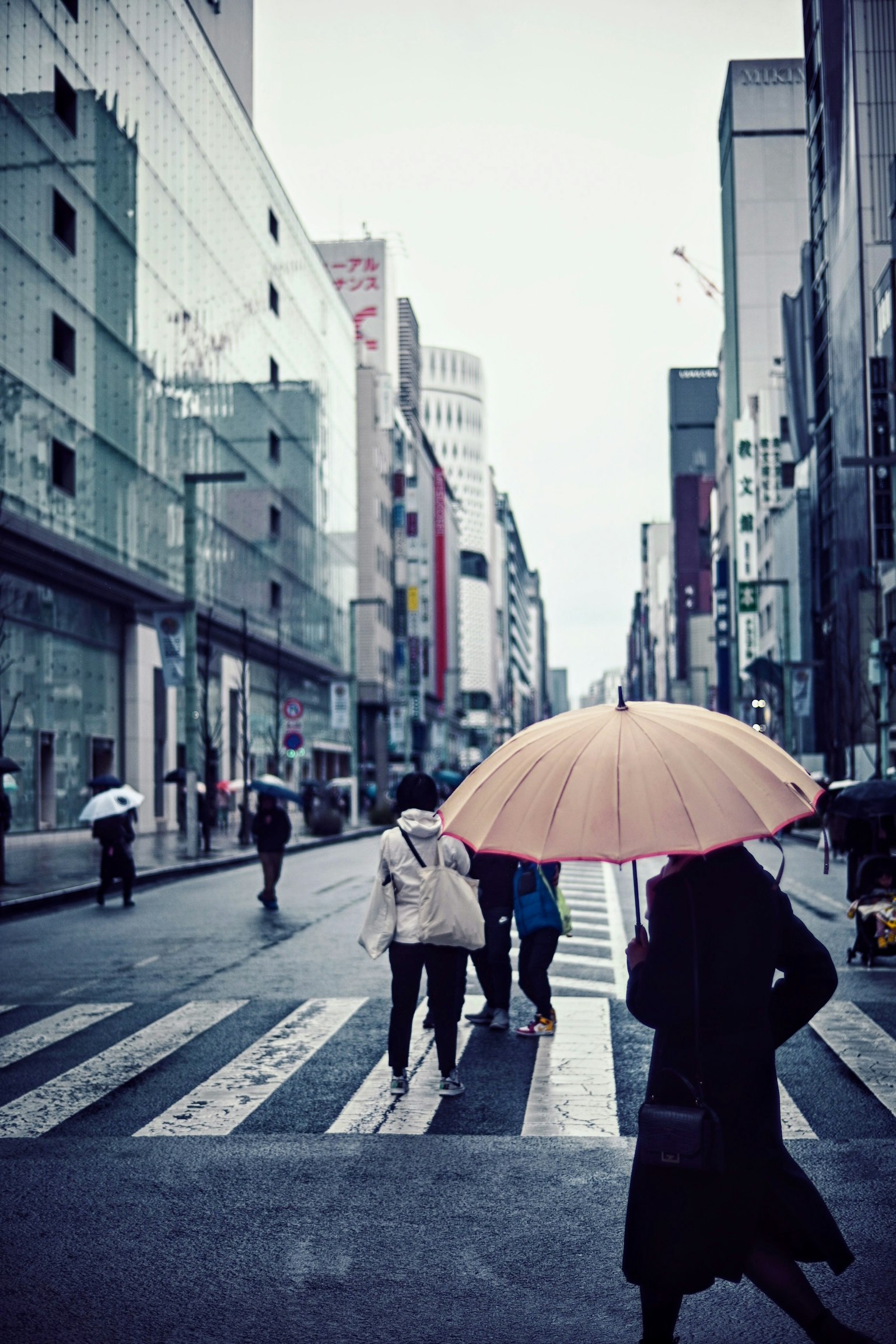 城市街道场景，人们在斑马线过马路，手持黄色雨伞的女性格外显眼