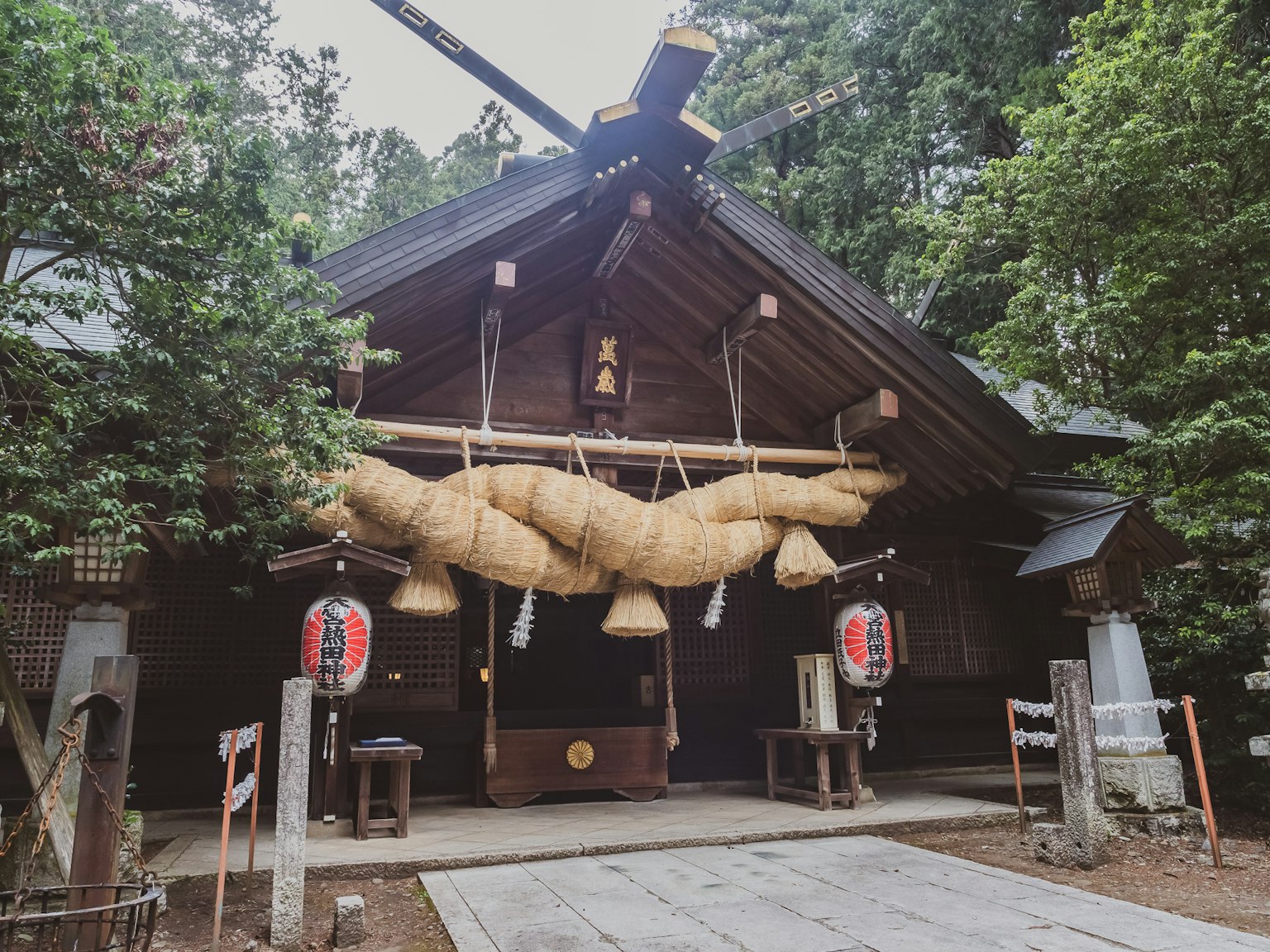 Traditional shrine building surrounded by greenery large straw decorations at the entrance