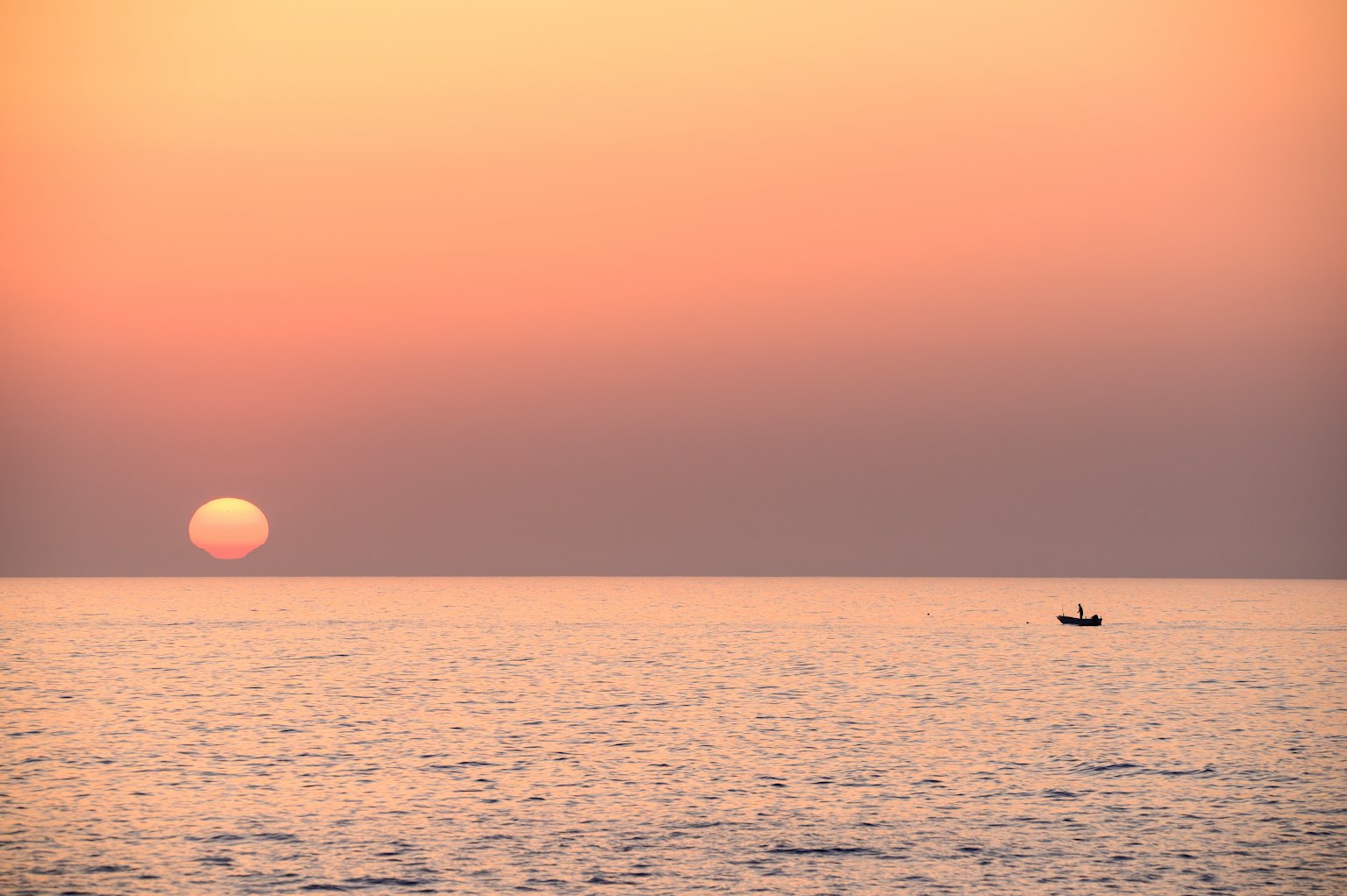 Serene sunset over calm sea with silhouette of small boat