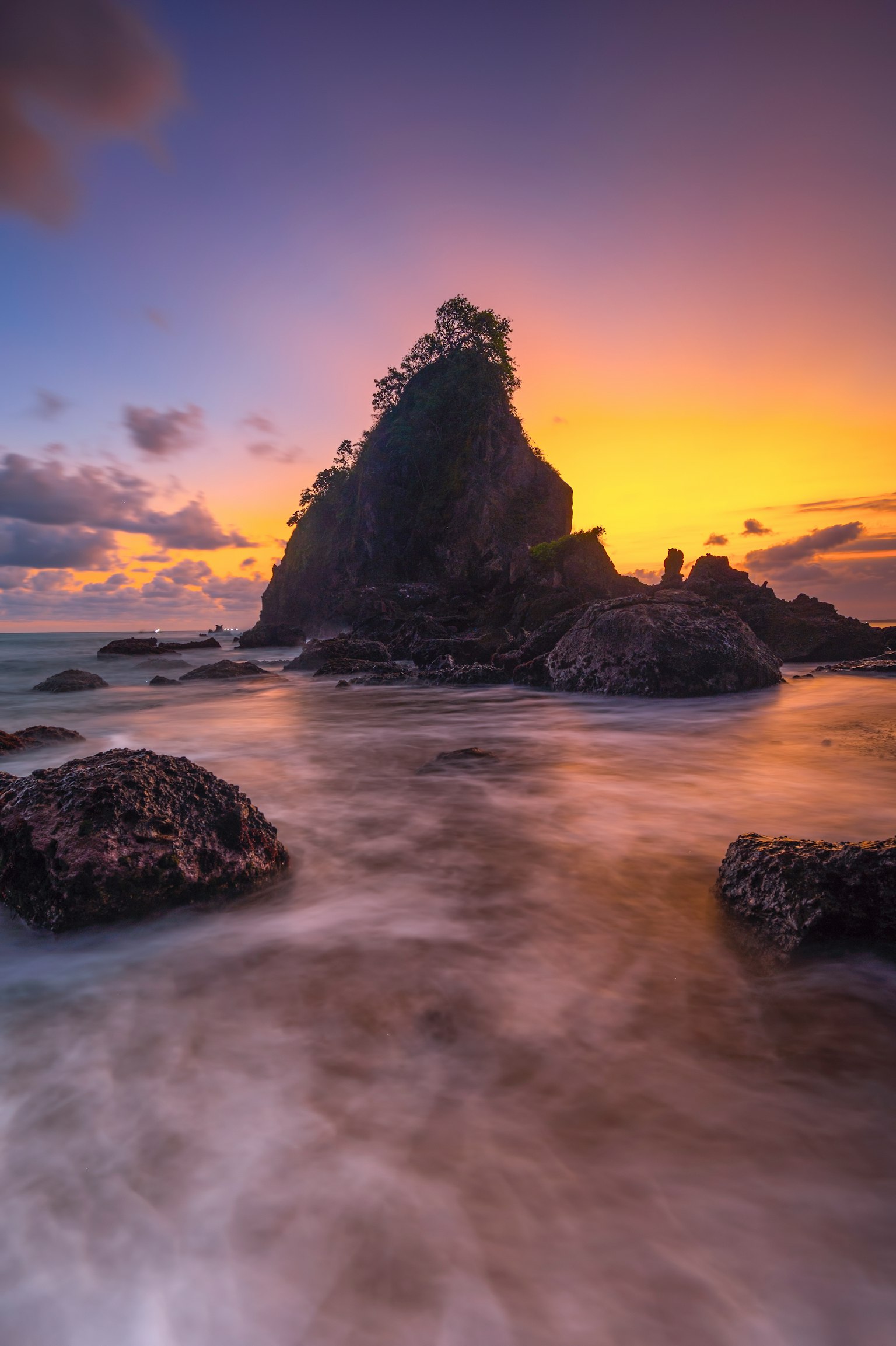 Grande roccia su una spiaggia al tramonto con onde calme