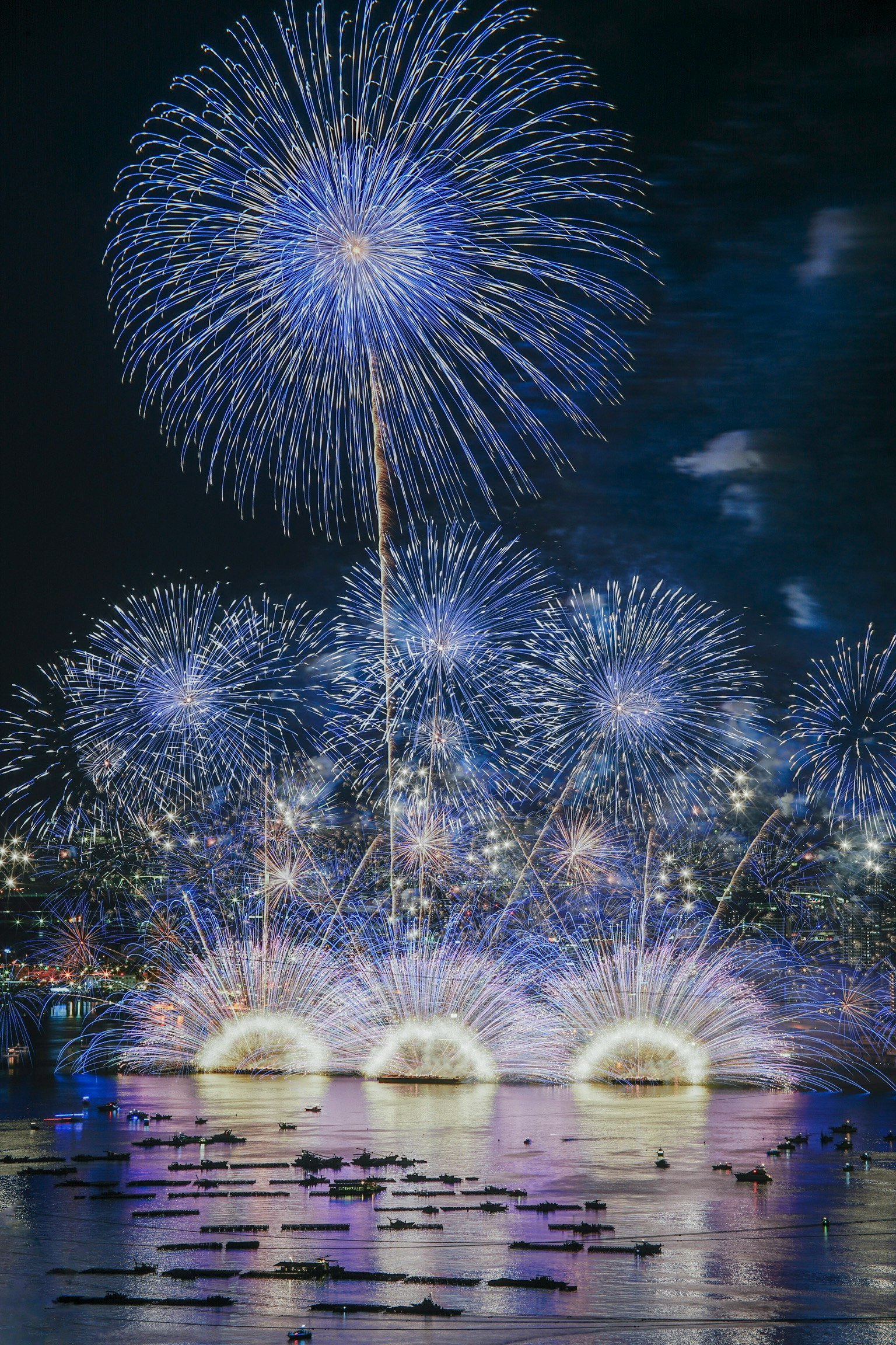 A vibrant display of blue fireworks lighting up the night sky reflections visible on the water surface