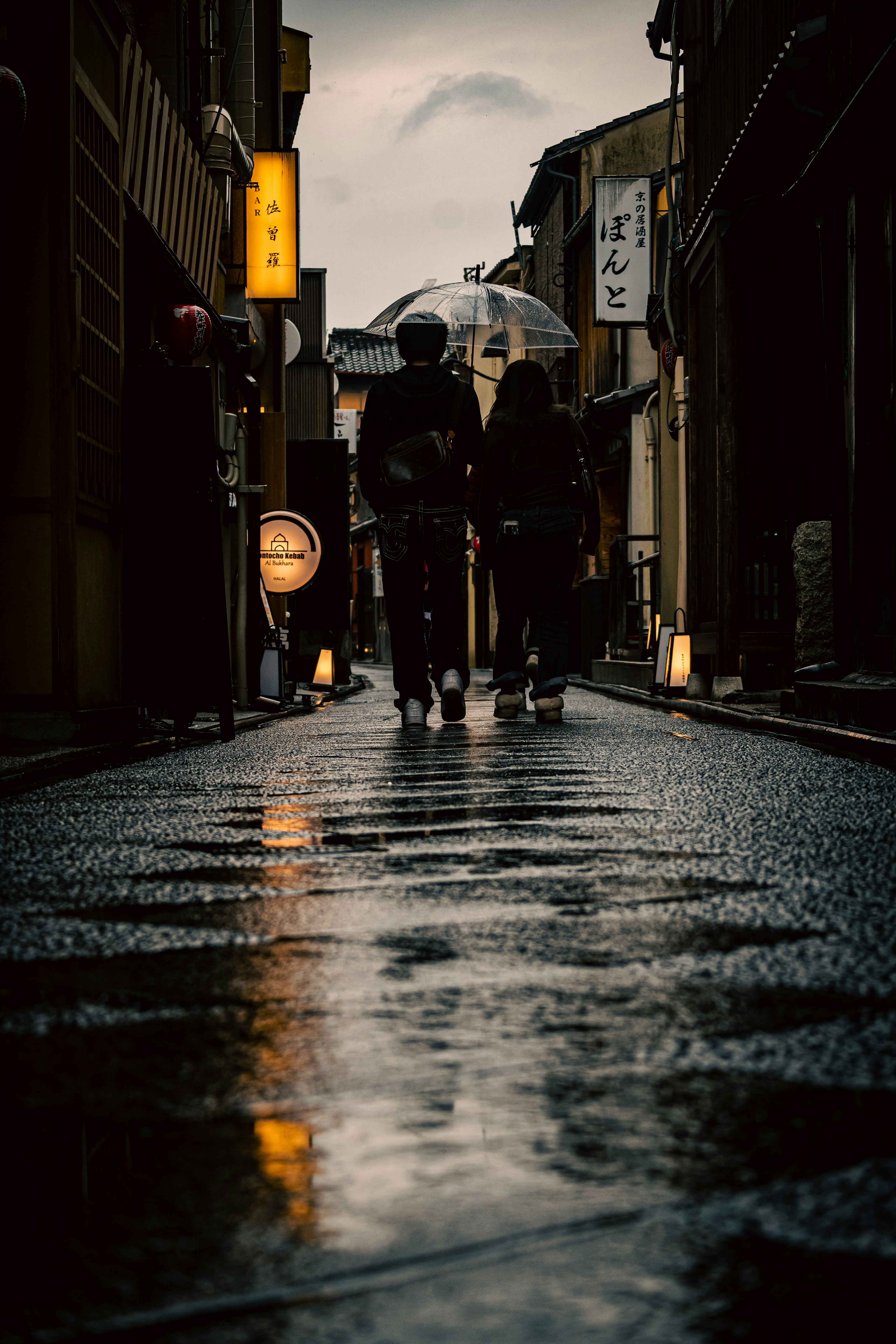 雨上がりの路地に並ぶ提灯と人影のある商店街