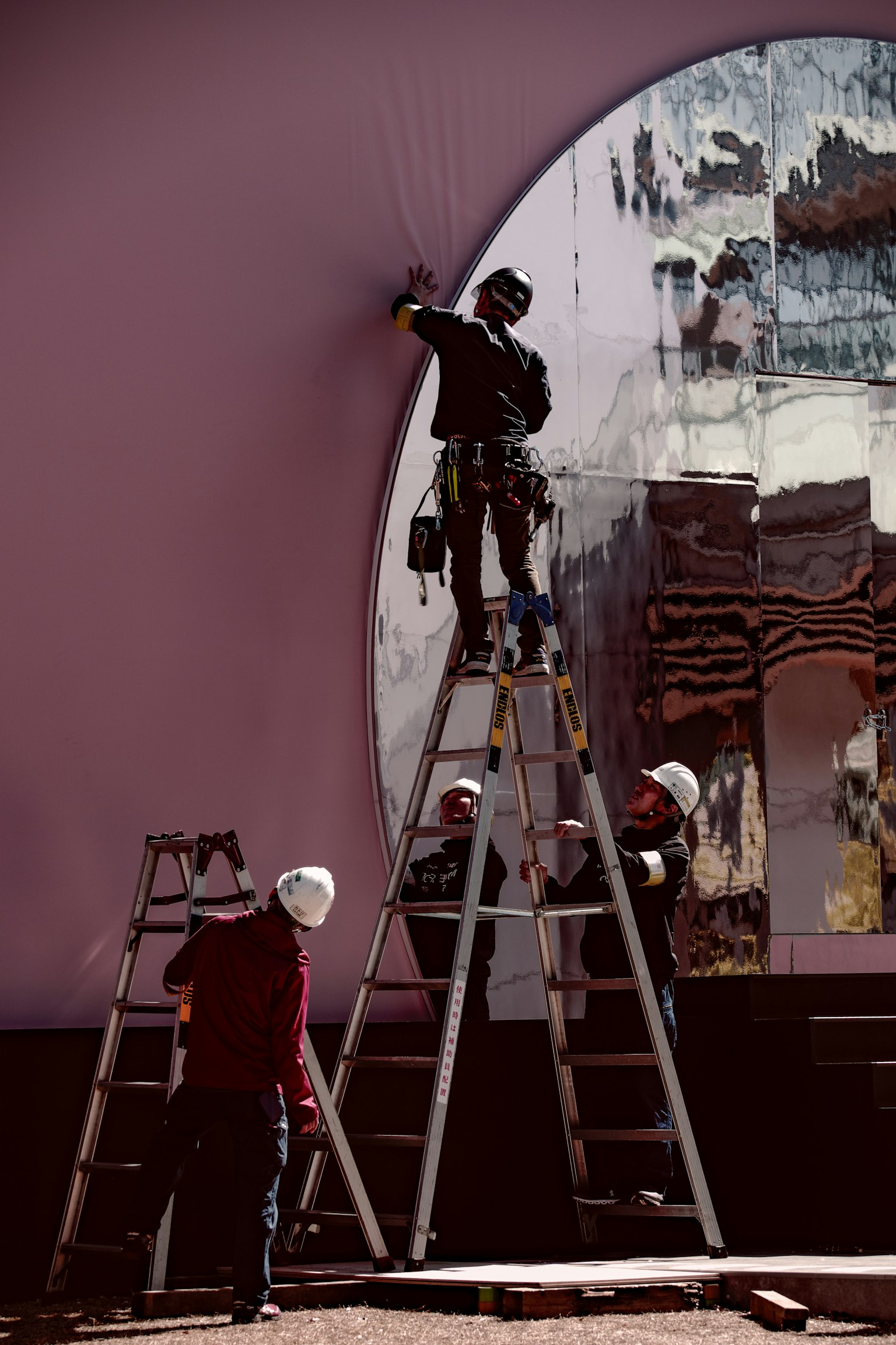Travailleurs sur un chantier avec un mur rose et une œuvre d'art miroir
