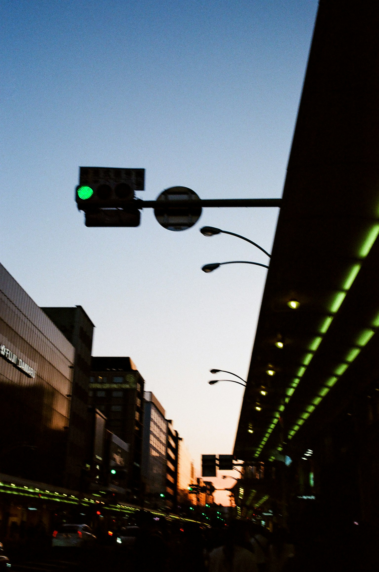 Scena di strada con un semaforo verde sotto un cielo al tramonto che presenta edifici urbani e lampioni illuminati