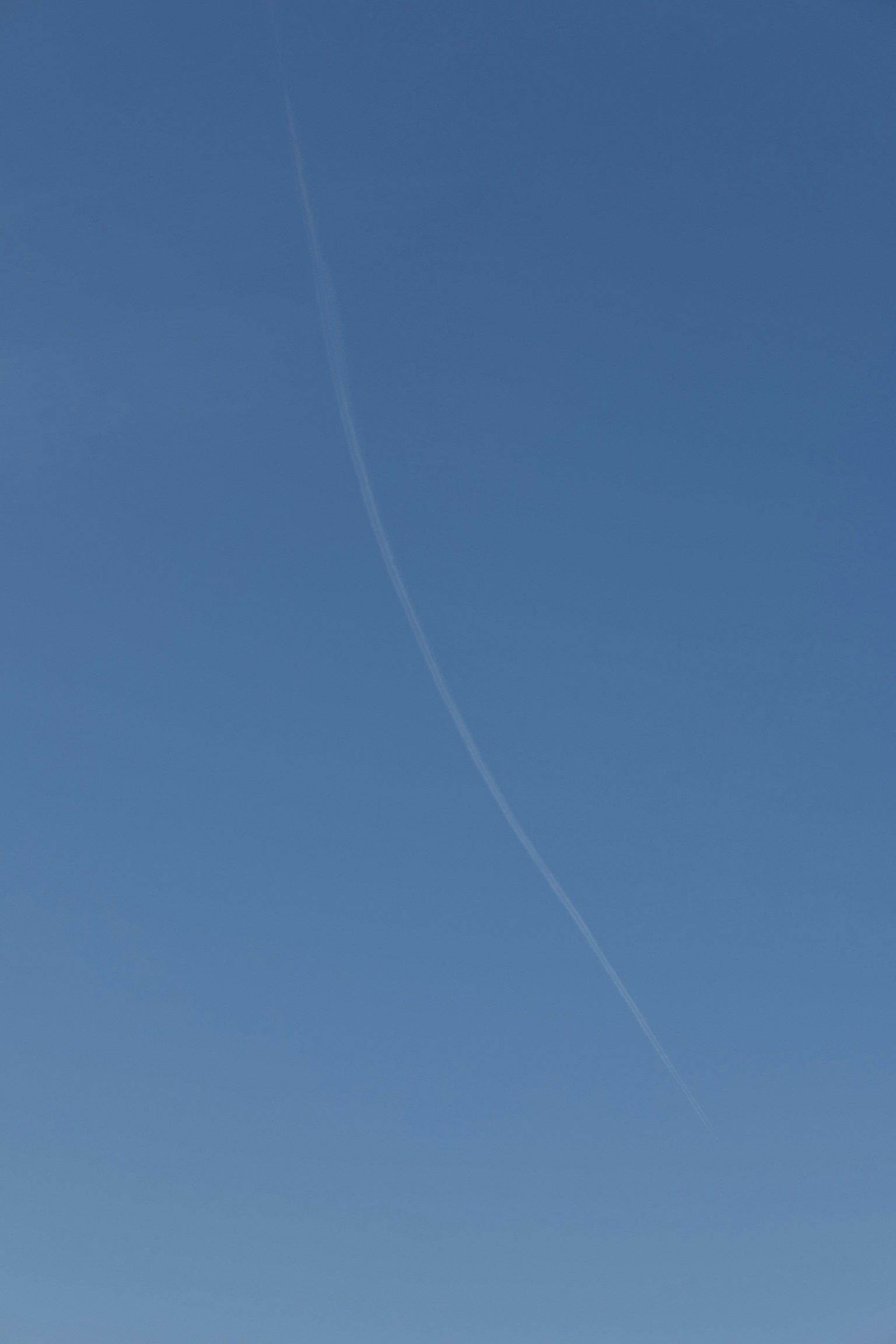 Traînée de condensation blanche courbée dans un ciel bleu clair