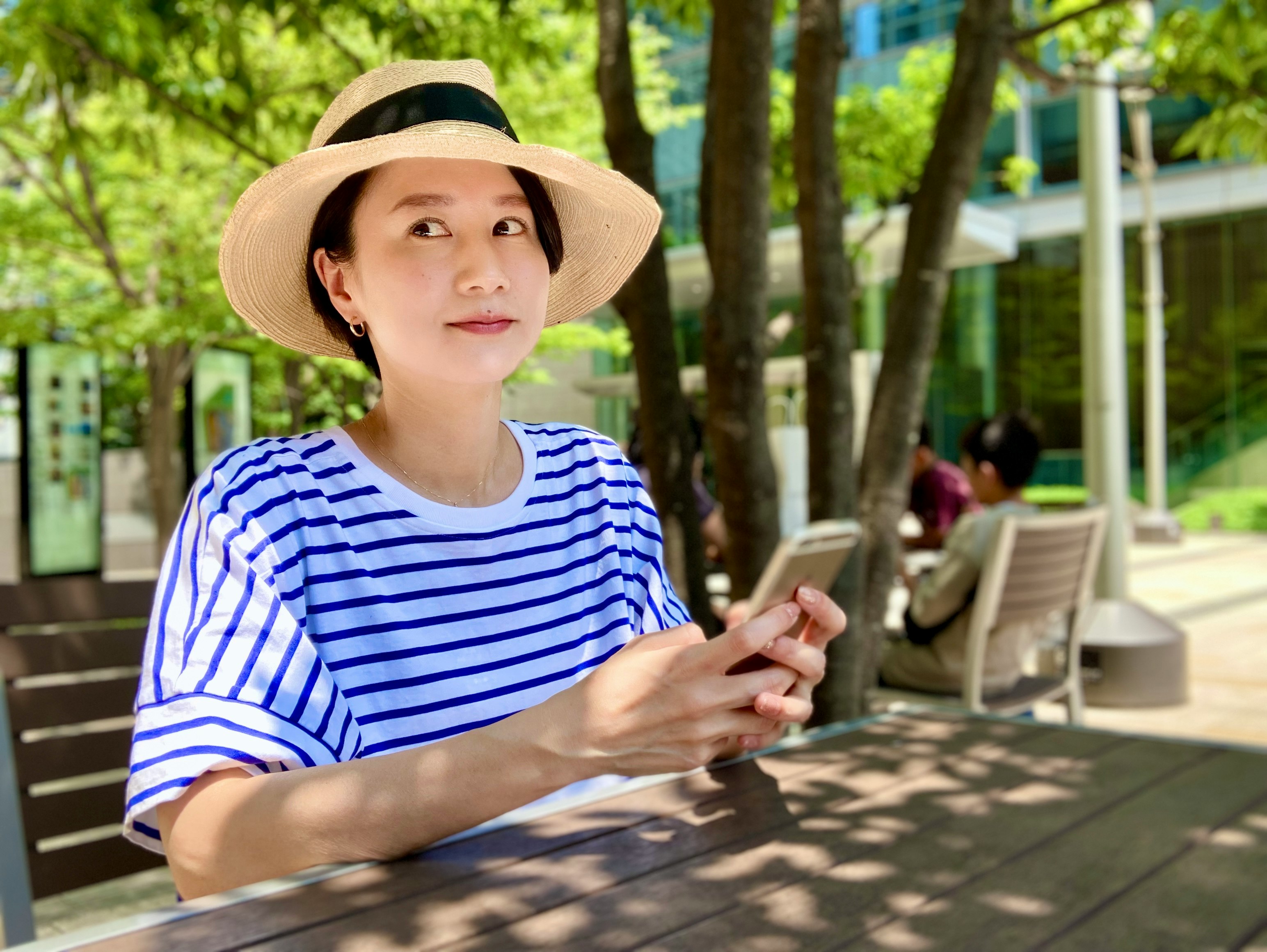 Frau schaut auf ein Smartphone auf einer Bank im Schatten