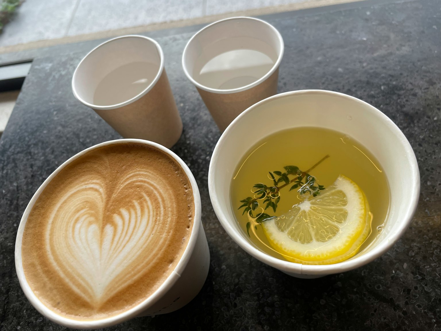 Café avec art de latte en forme de cœur et une boisson avec une tranche de citron et des herbes