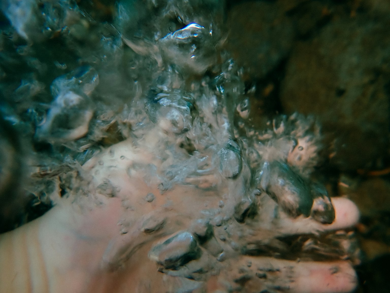 Image of a hand underwater with visible stones and rippling water