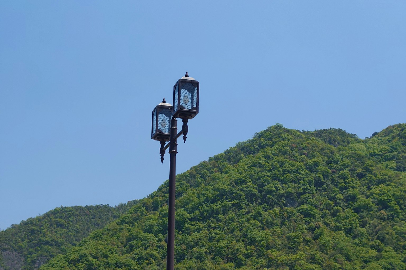 Zwei Laternen im lanternenstil vor einem Hintergrund von üppigen grünen Bergen unter einem klaren blauen Himmel
