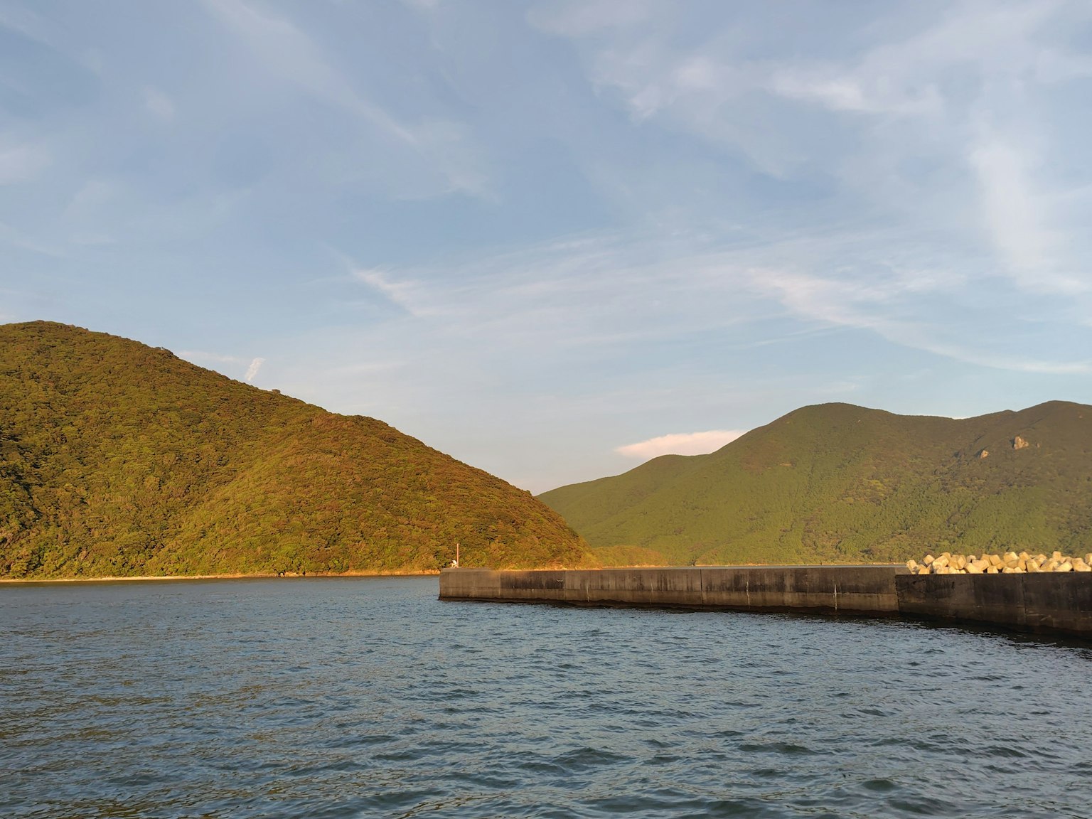 Malersicher Blick auf ruhiges Meer und grüne Berge mit einem Hafenpier