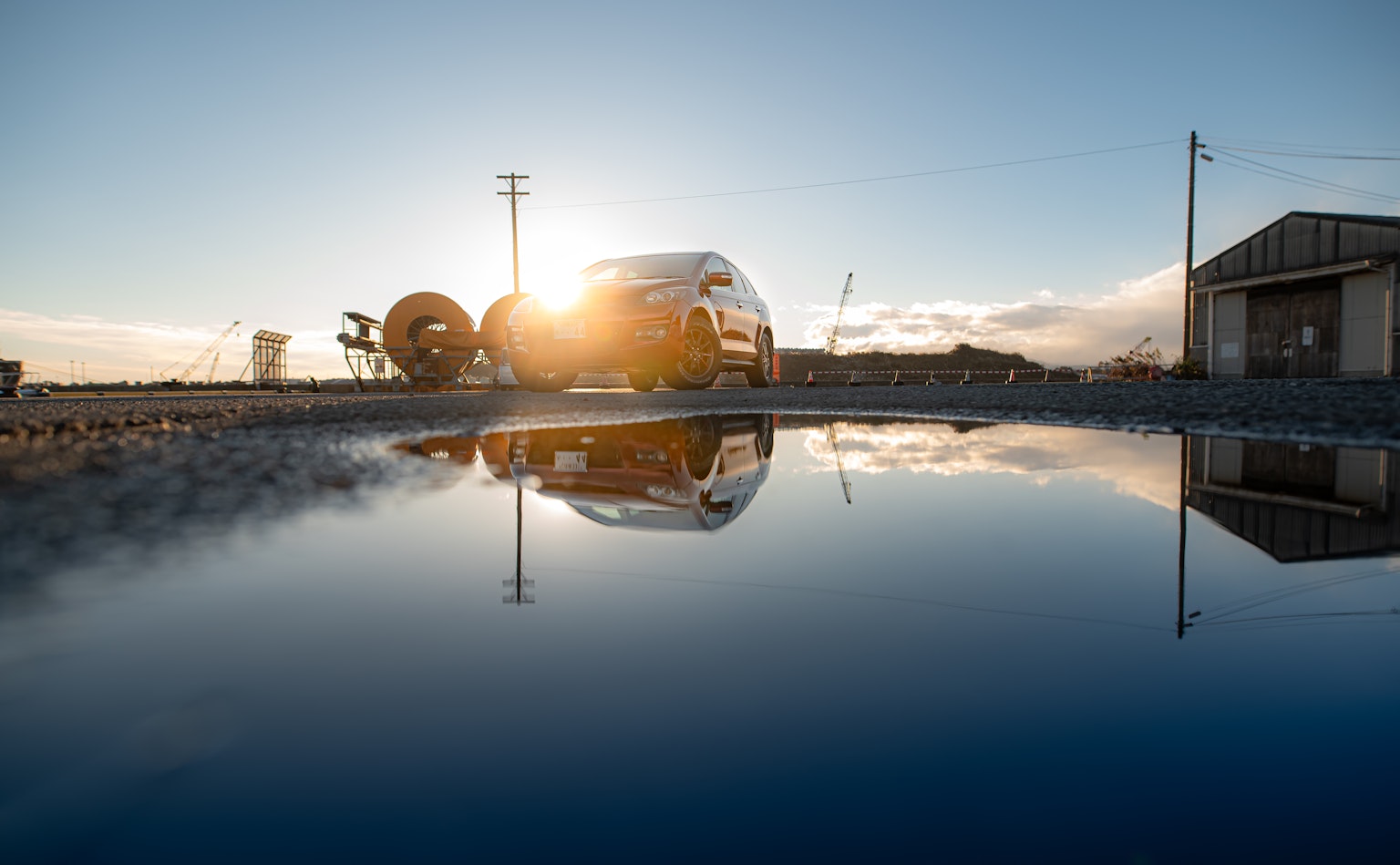 Un vehículo de trabajo y un edificio al lado de un charco que refleja el atardecer