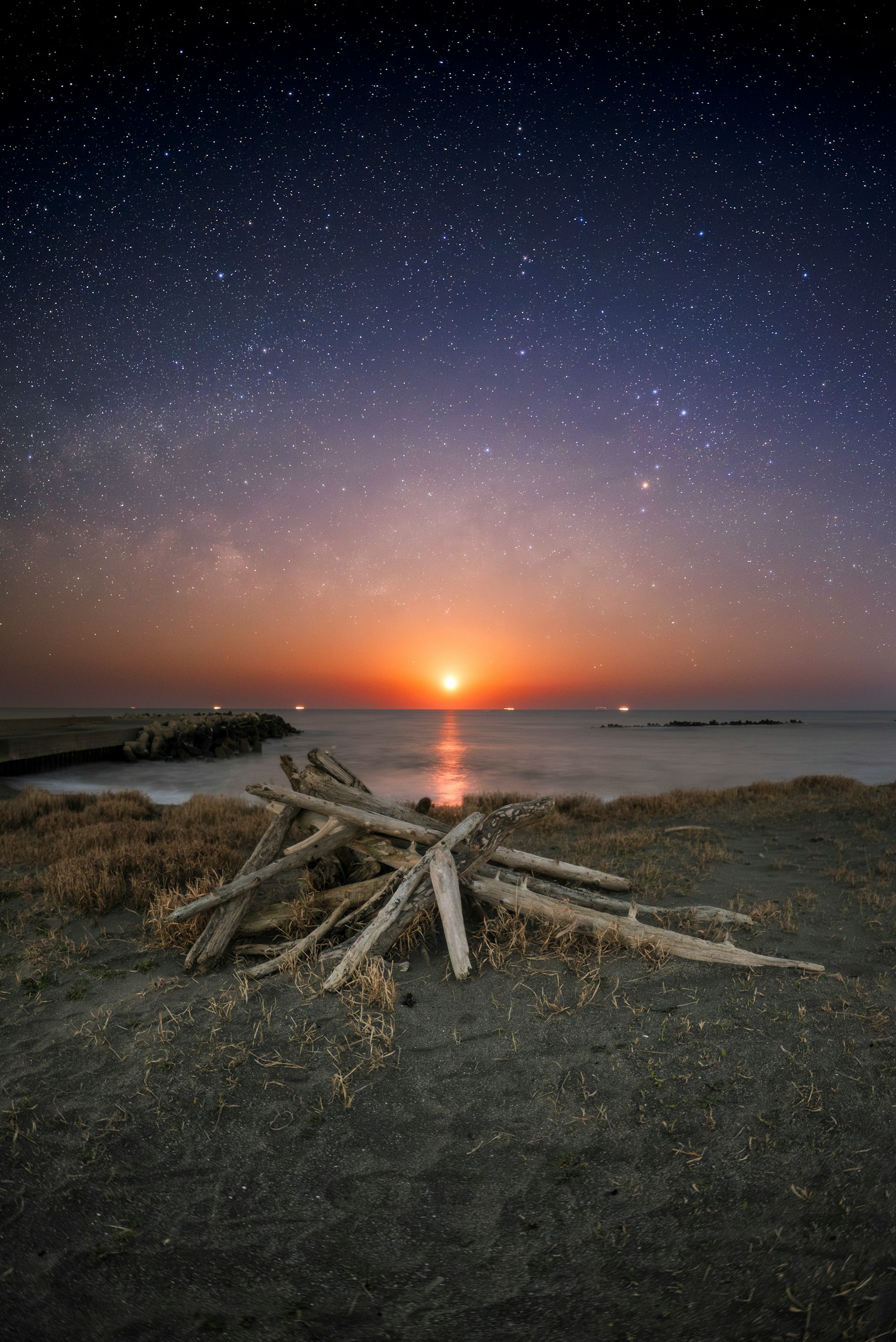 Un cumulo di legno sulla spiaggia con un tramonto e un cielo stellato sullo sfondo