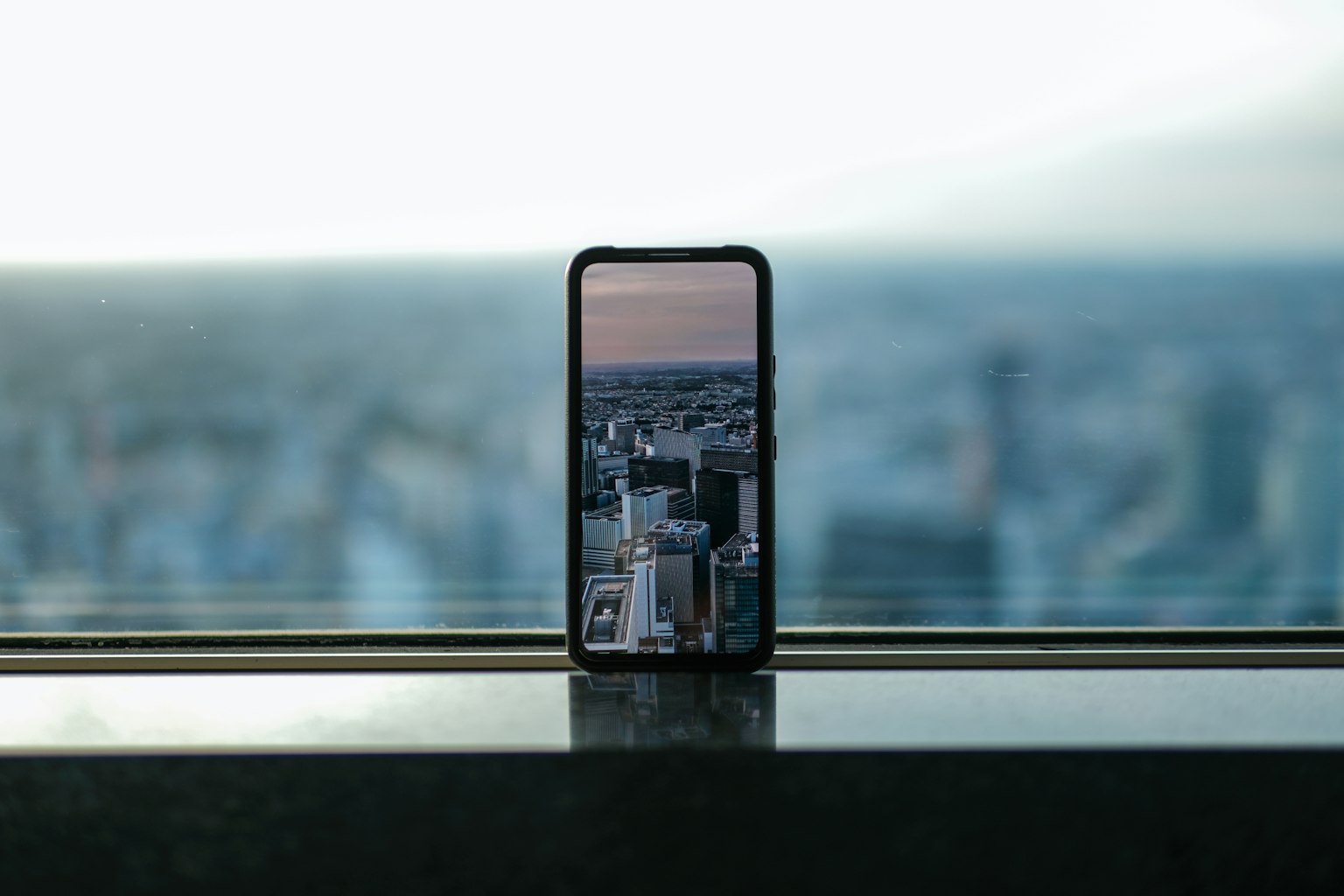 Smartphone yang menampilkan pemandangan kota diletakkan di ambang jendela