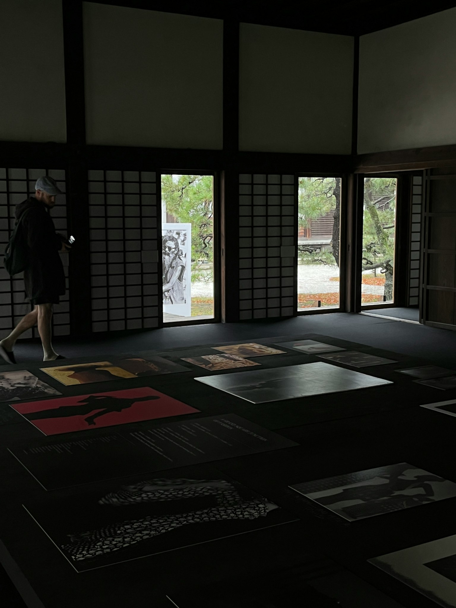 A dimly lit room with artworks spread across the floor and a woman walking