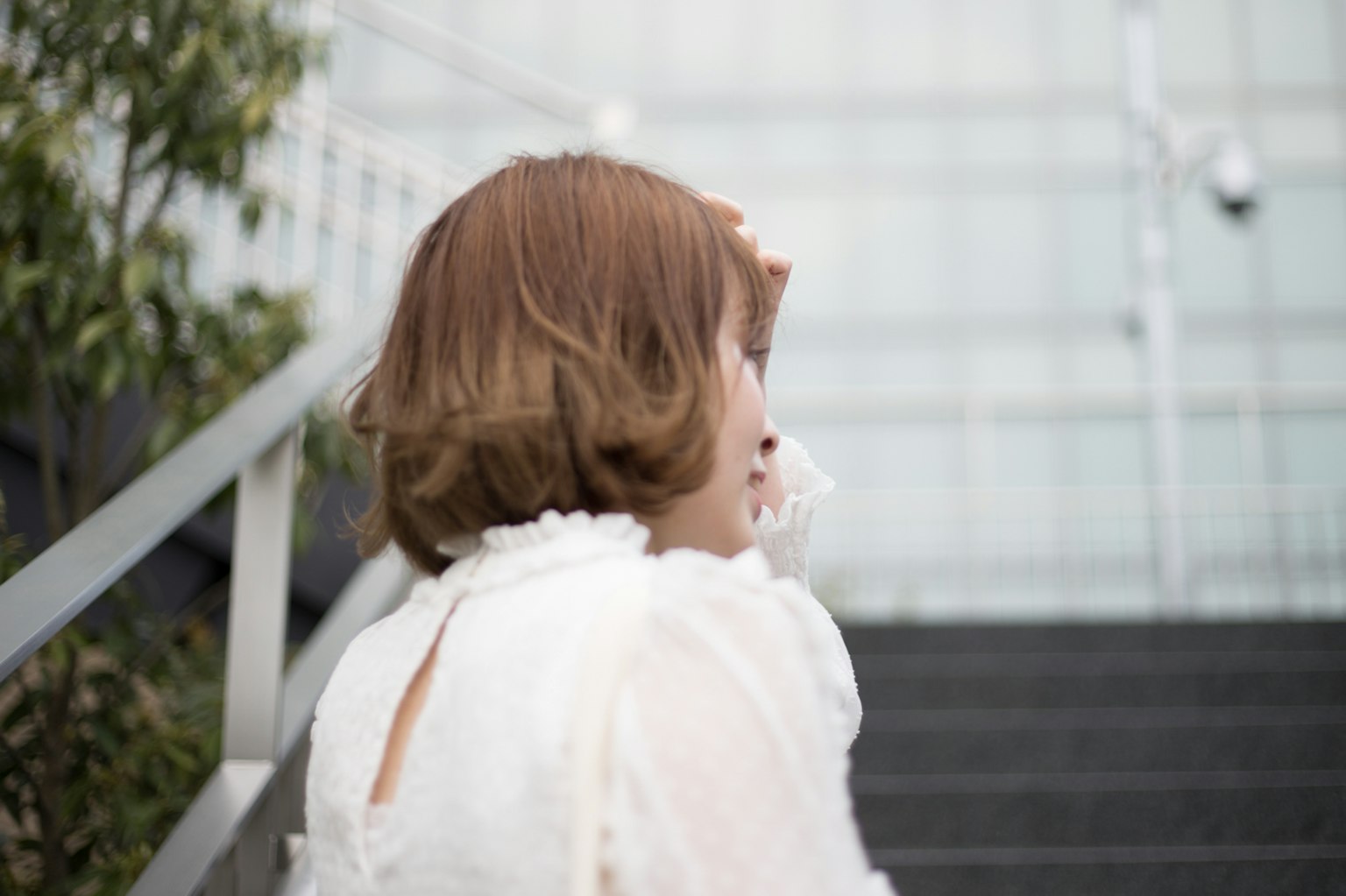 계단을 오르는 여성의 뒷모습 짧은 갈색 머리 흰색 블라우스 녹색 식물로 둘러싸임