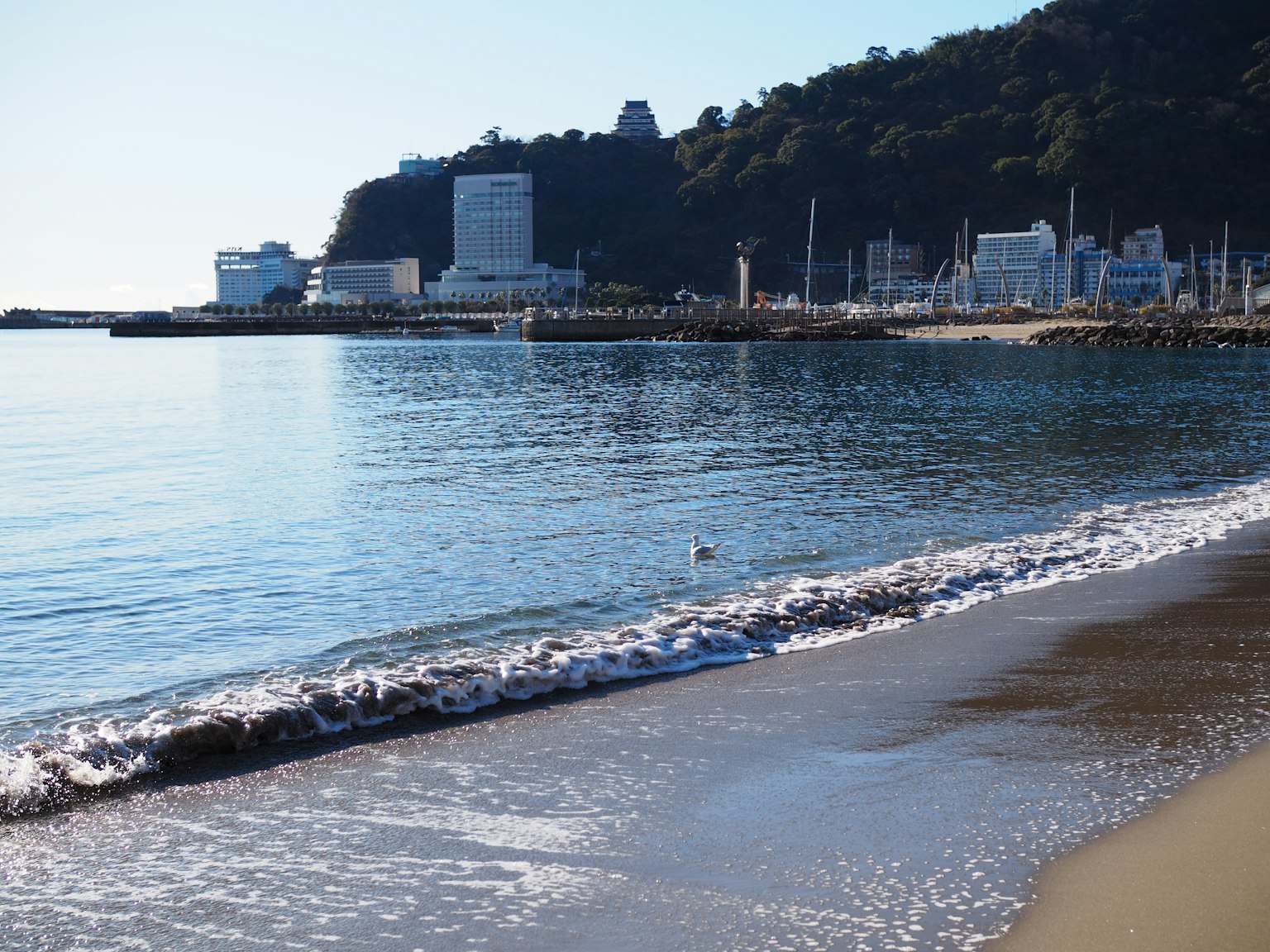 Scena di mare calmo e spiaggia di sabbia Edifici portuali e montagna sullo sfondo
