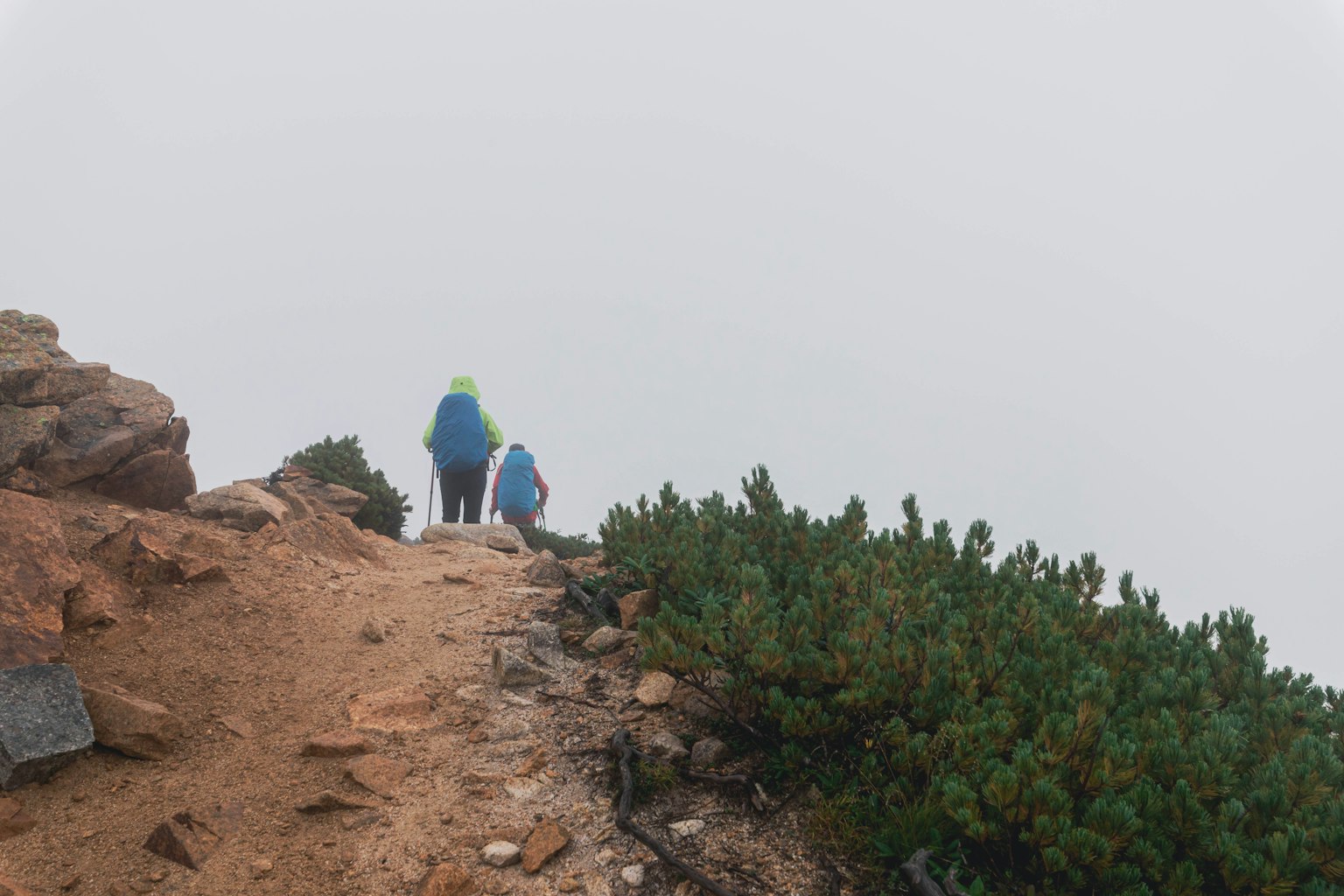 Two hikers walking in fog along a rocky path