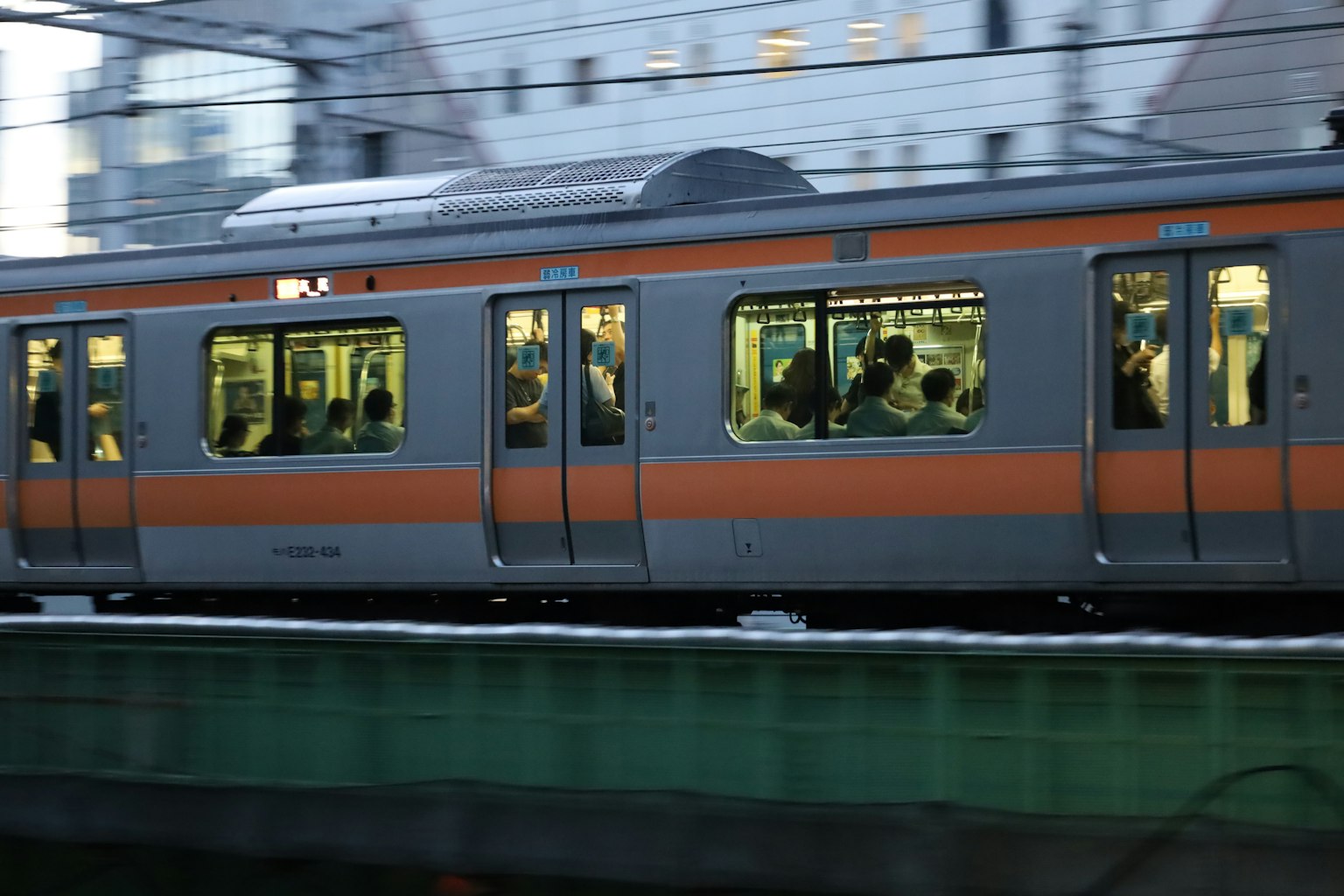一列帶有橙色條紋的火車在運動中，窗戶裡可見乘客