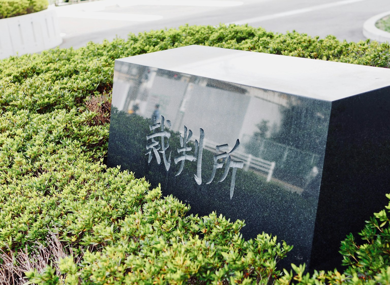 一块黑色石碑上刻有日文字符，周围环绕着绿色灌木