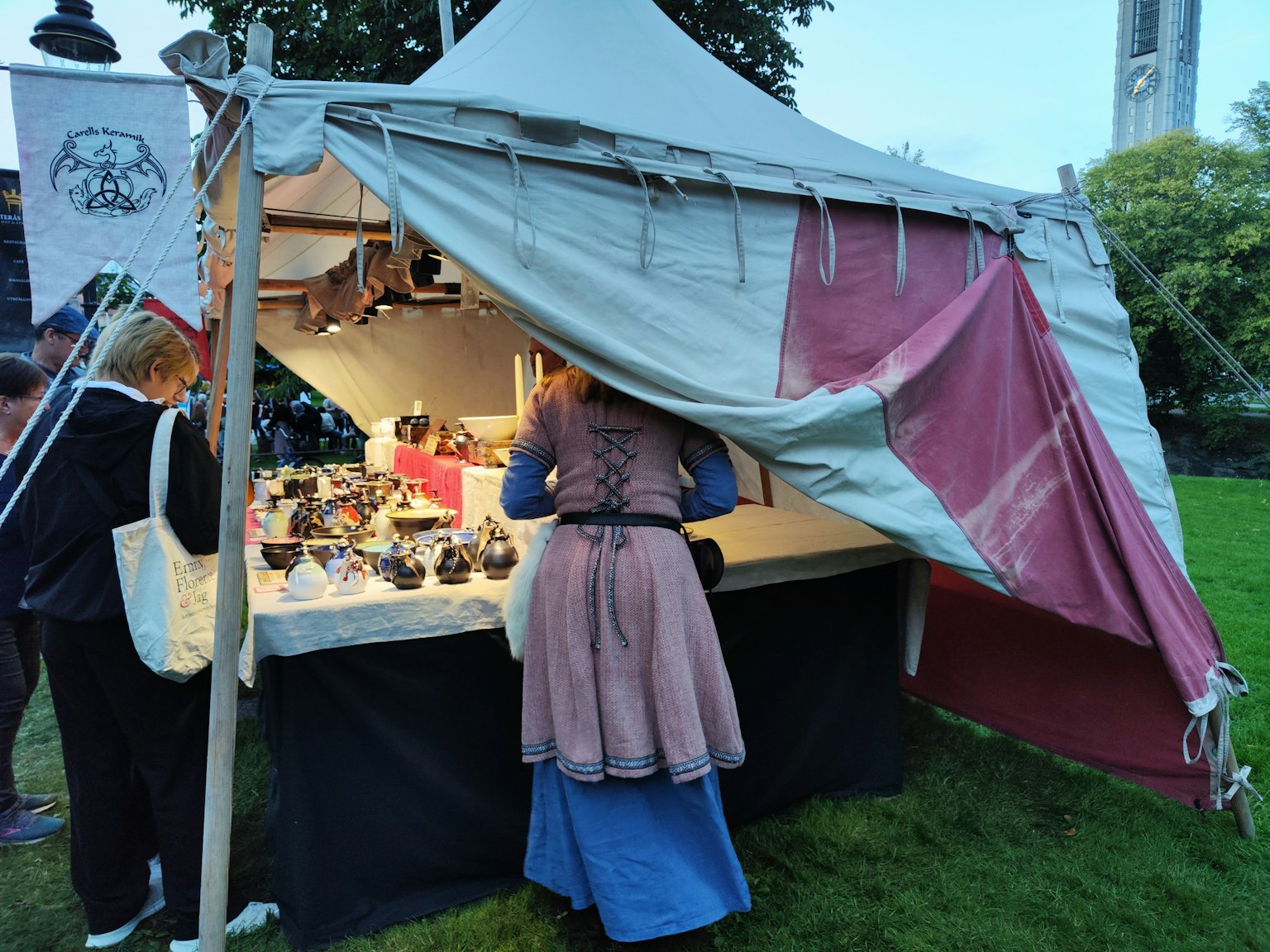 Frau, die Artikel an einem Marktstand mit einem Zelt im Hintergrund betrachtet