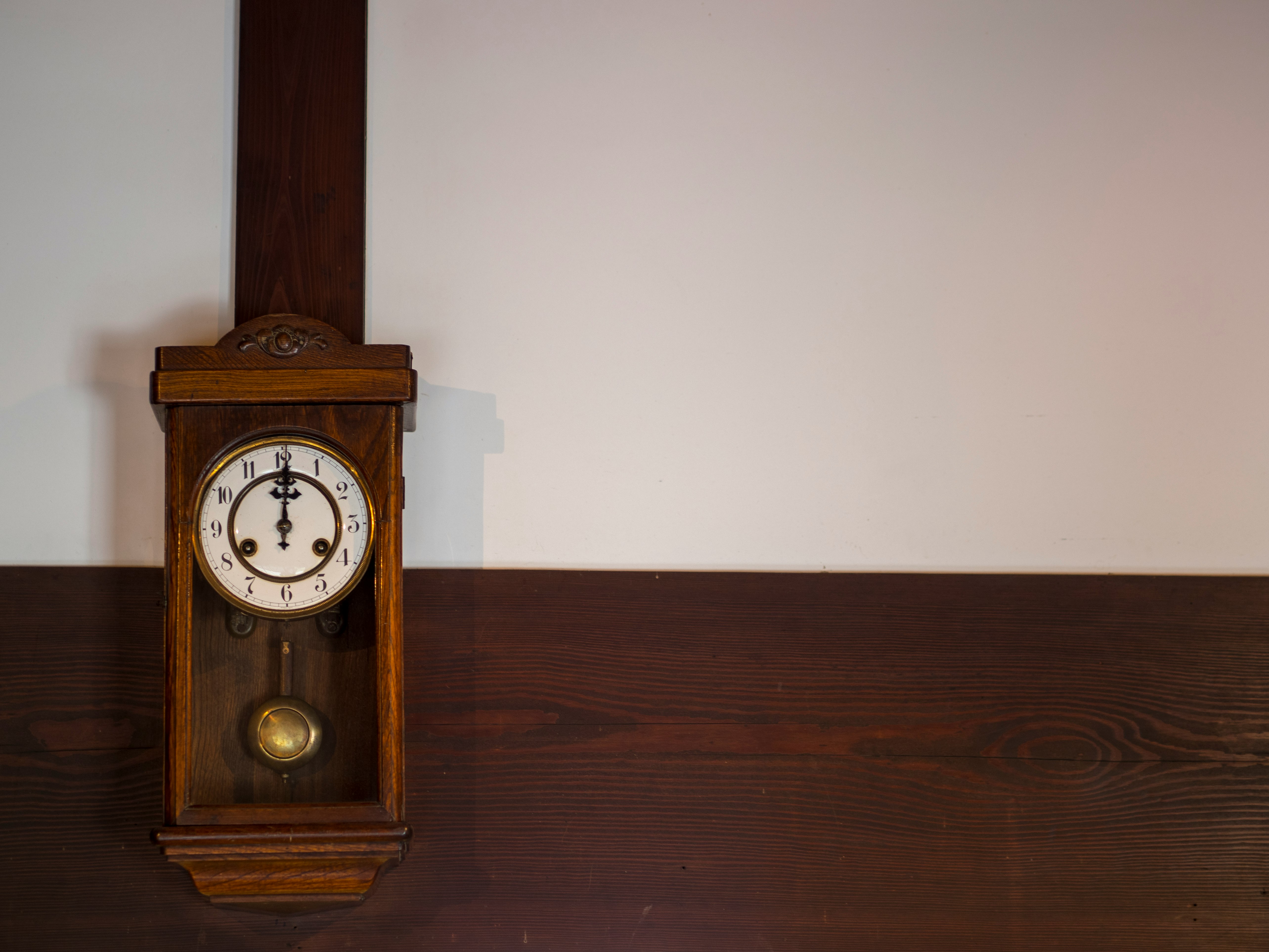 wooden pendulum clock placed against a wall in an indoor room
