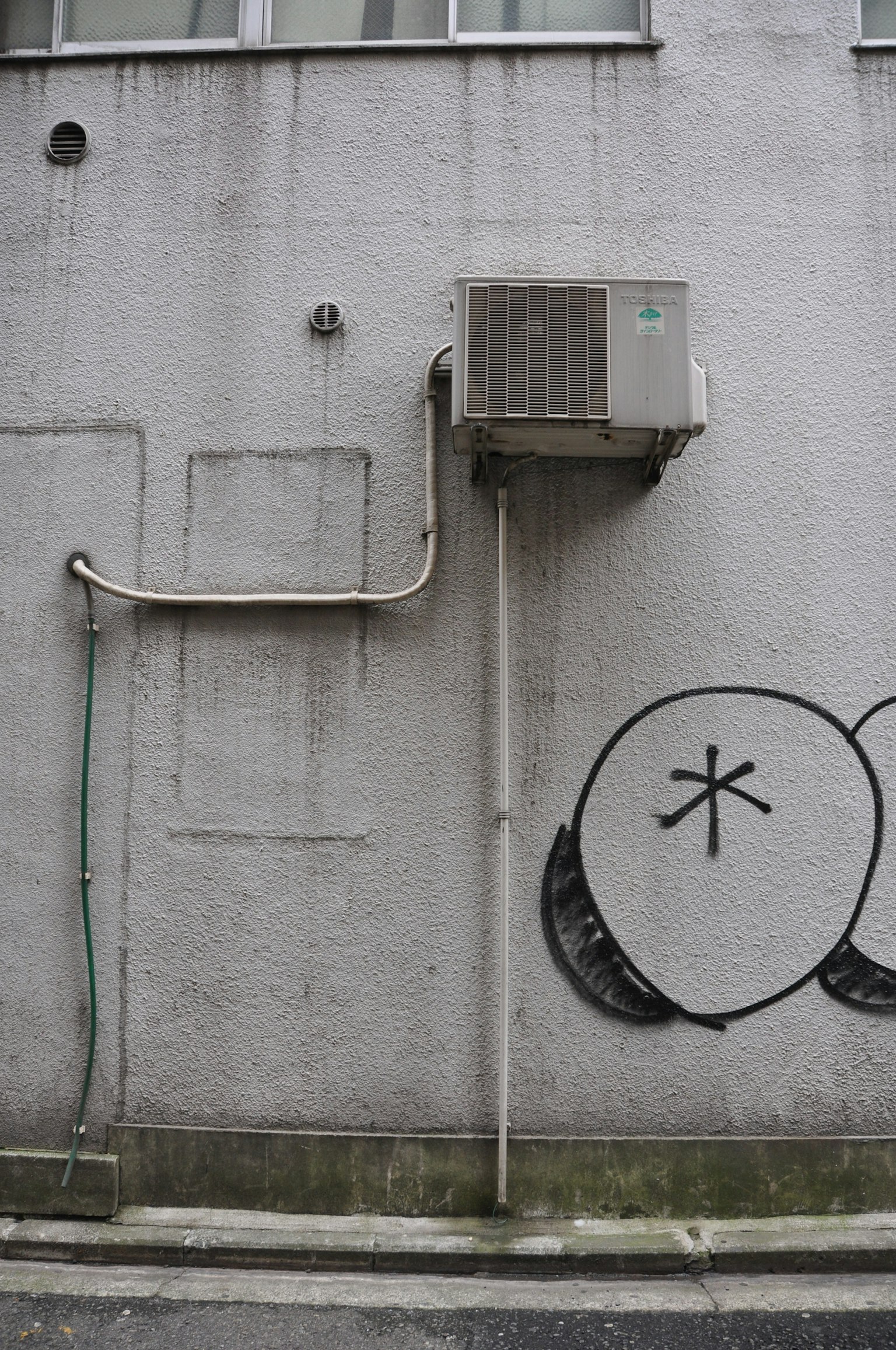 Dinding abu-abu dengan AC terpasang dan grafiti bulat hitam
