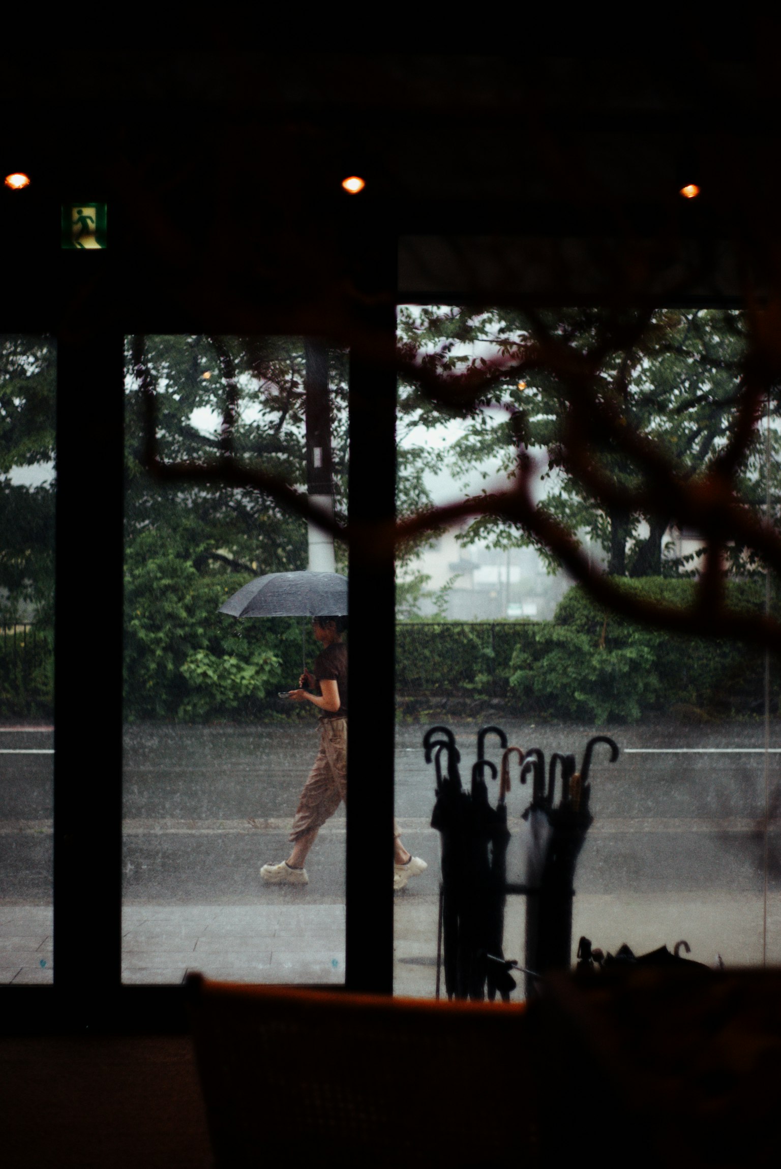 Una persona caminando con un paraguas bajo la lluvia vista a través de una ventana
