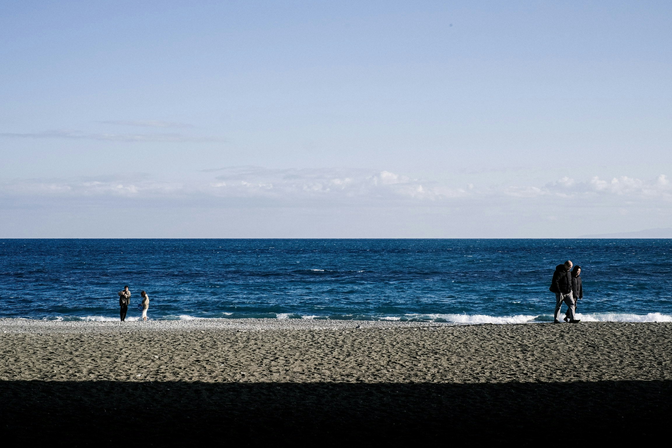冬の海辺で歩く人と広がる水平線