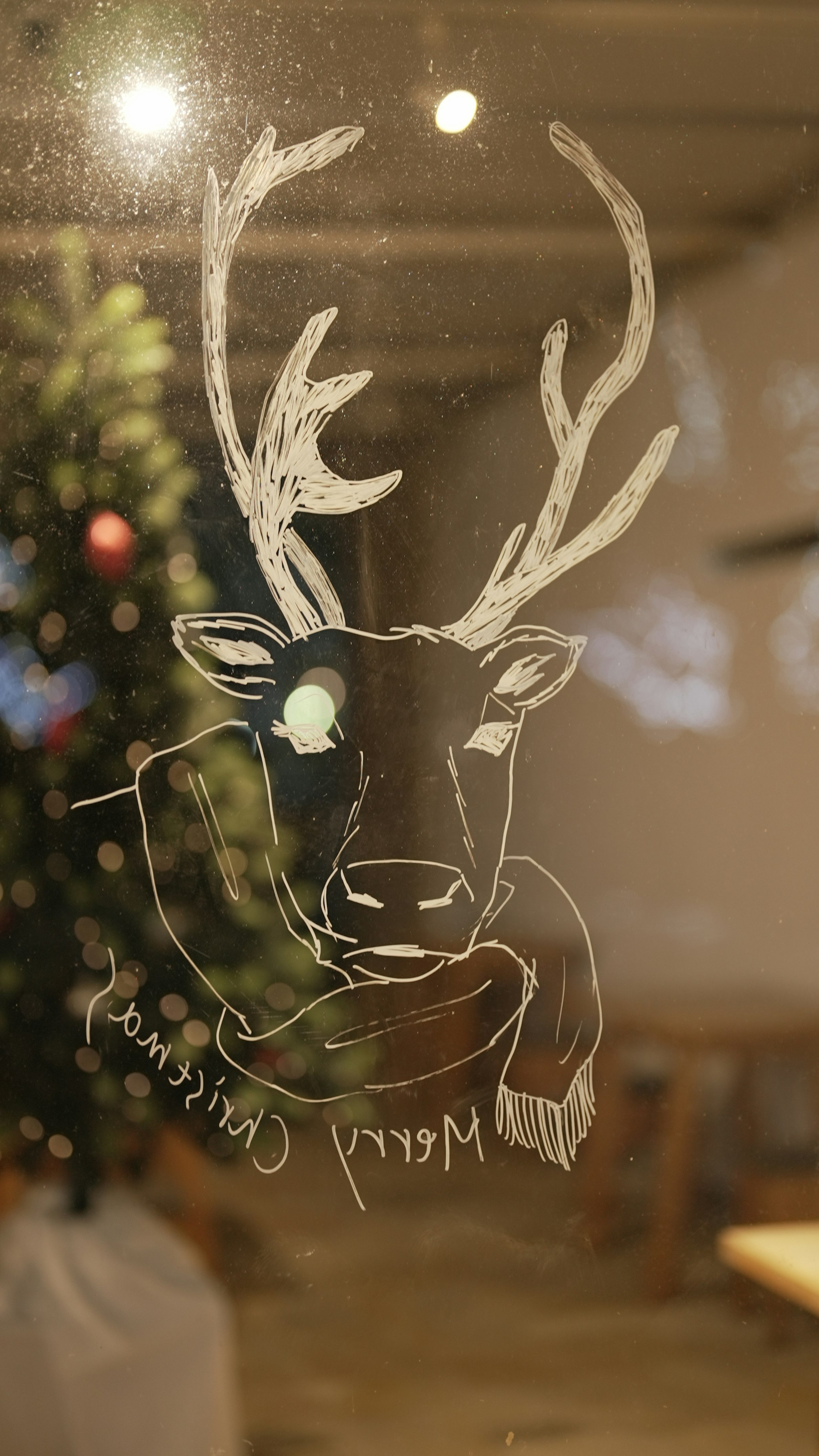 dessin au trait de renne sur une vitre avec des lumières intérieures chaudes