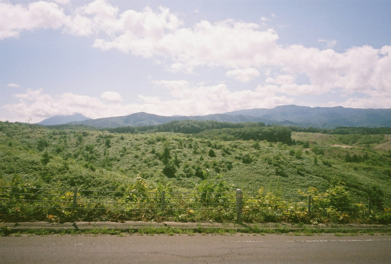 เนินเขาสีเขียวและภูเขาใต้ท้องฟ้าสีฟ้าพร้อมเมฆขาว